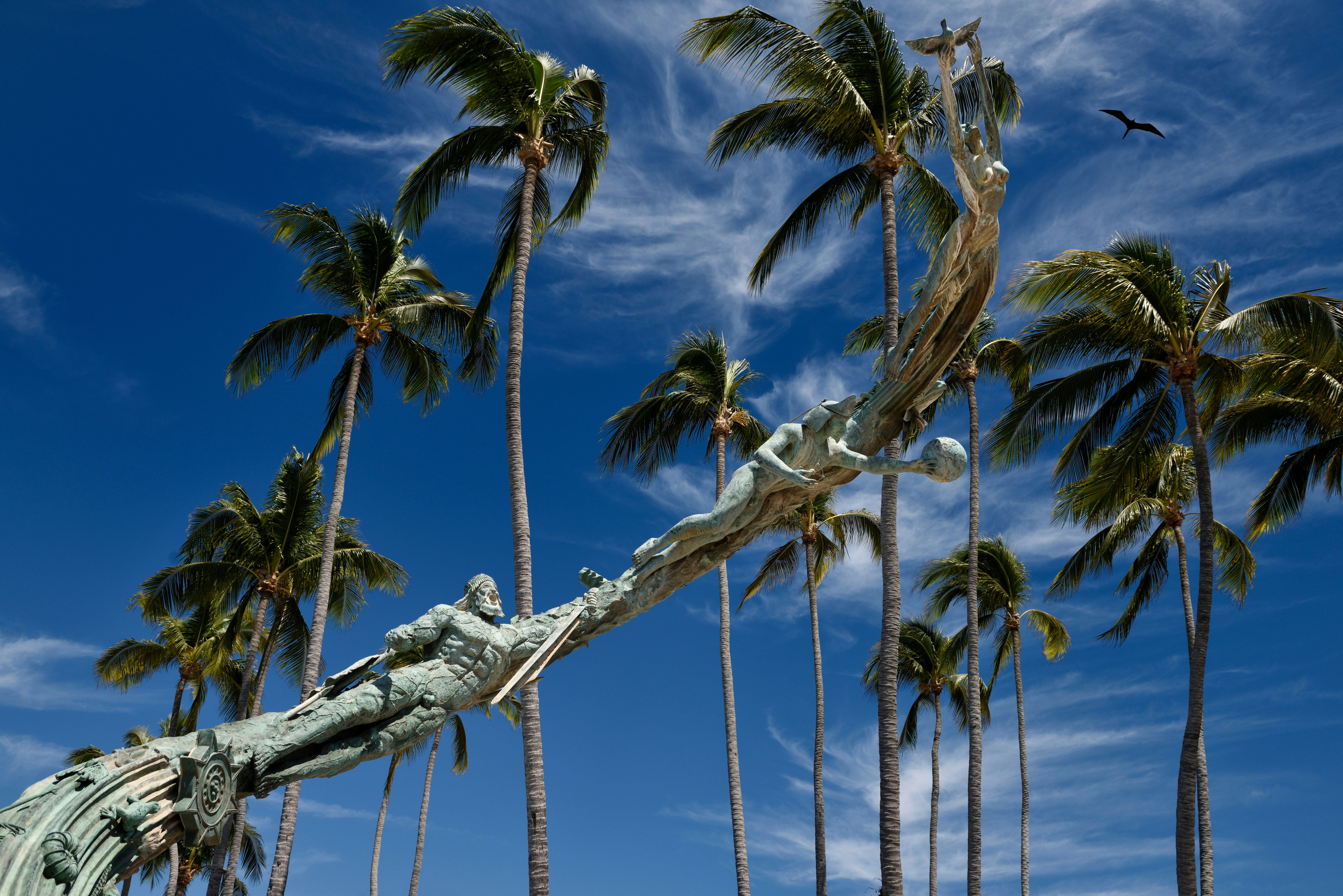 A bronze sculpture on the Malecón in Puerto Vallarta, Mexico, with palm trees behind.