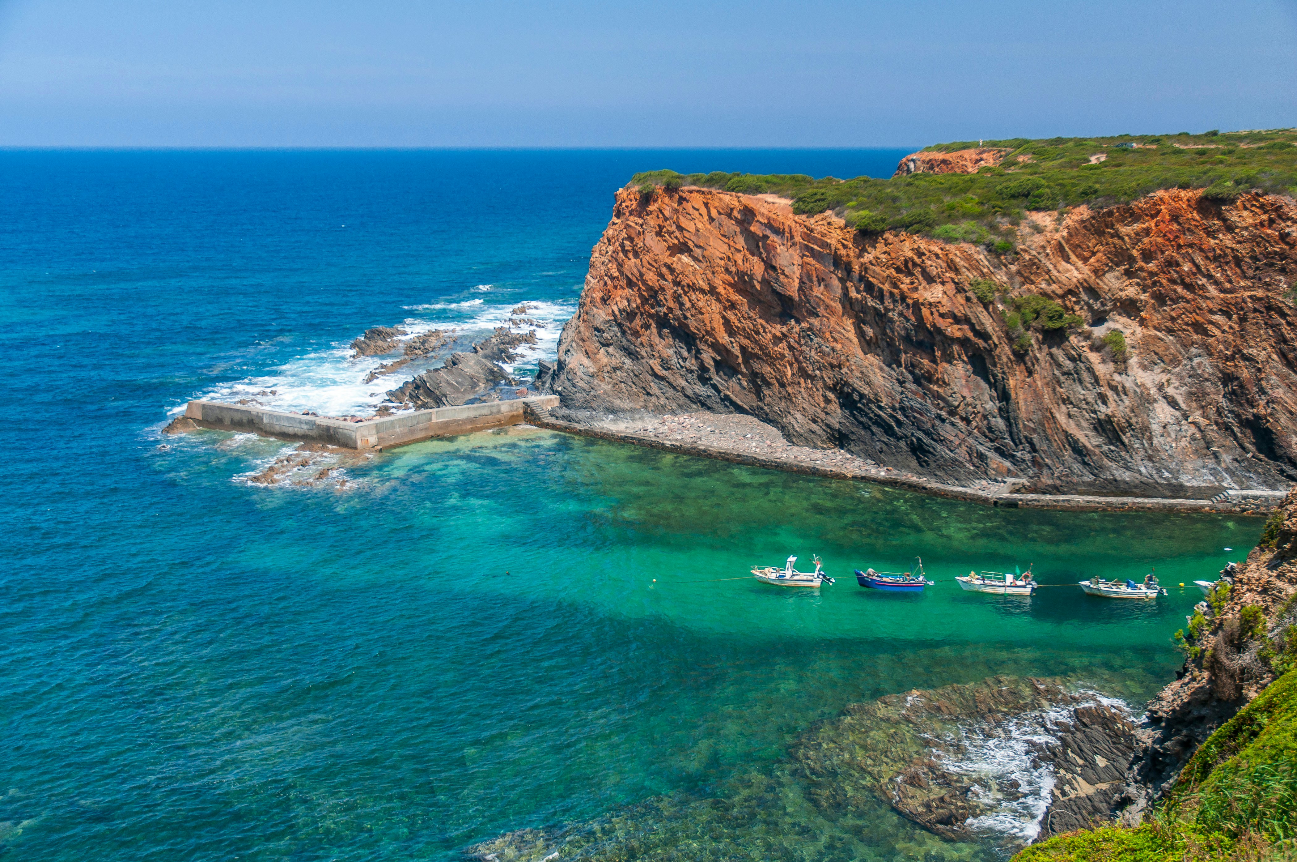 A narrow inlet between rocky cliffs, where five small boats have moored in the sheltered water.