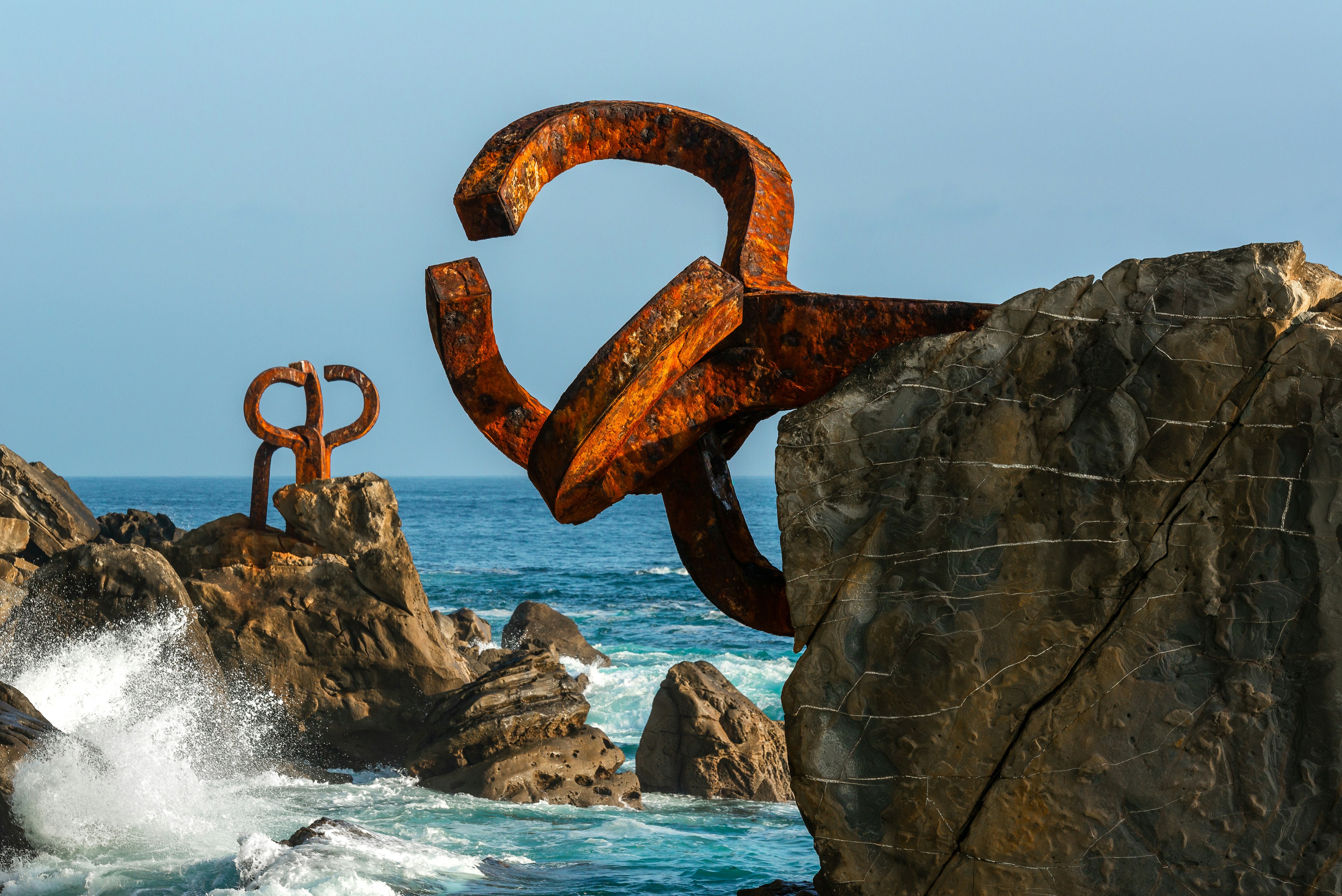 A rusted sculpture is embedded in rocks in the sea.