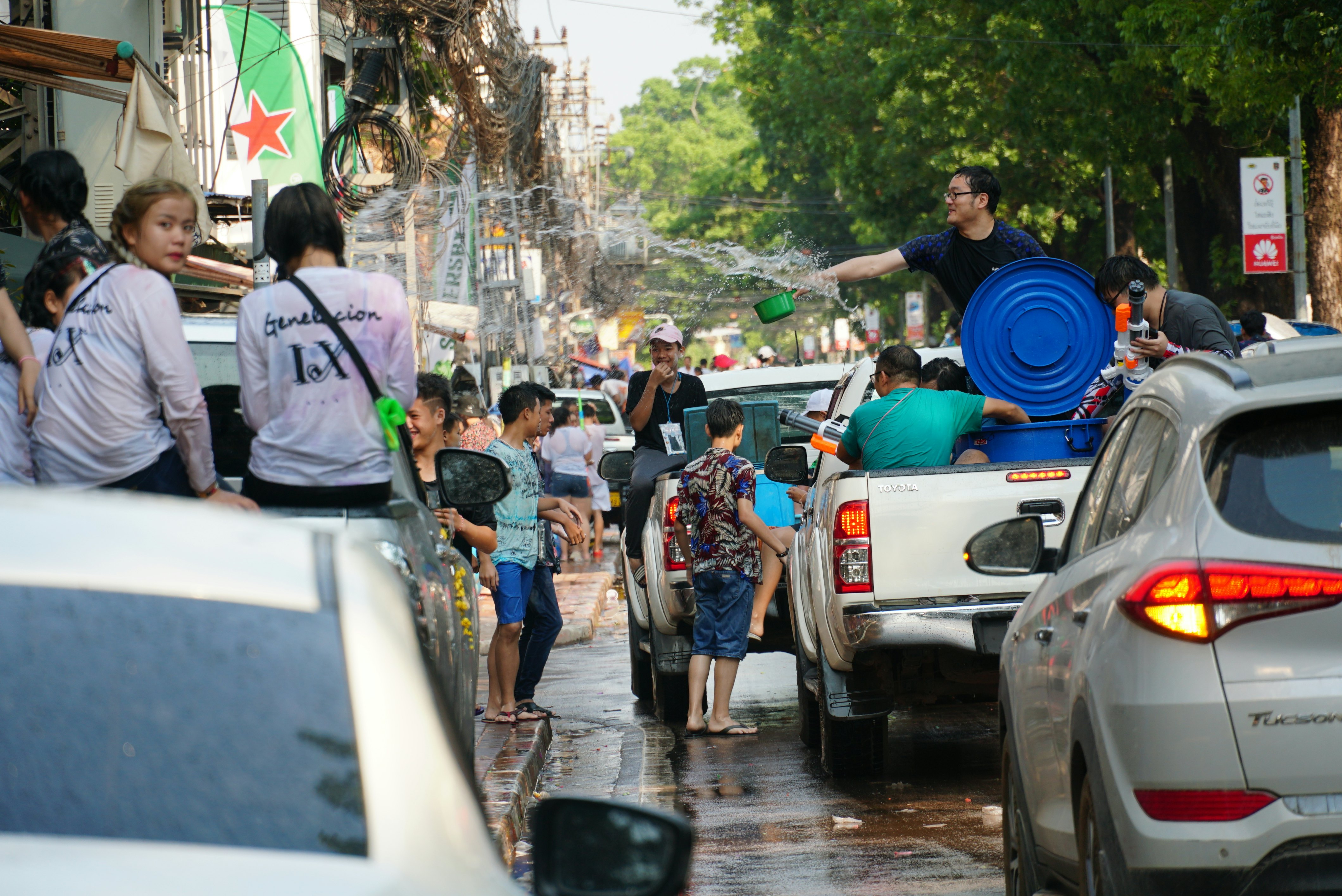 A man in the back of a pickup truck throws water onto a crowd in a city street during a celebration.