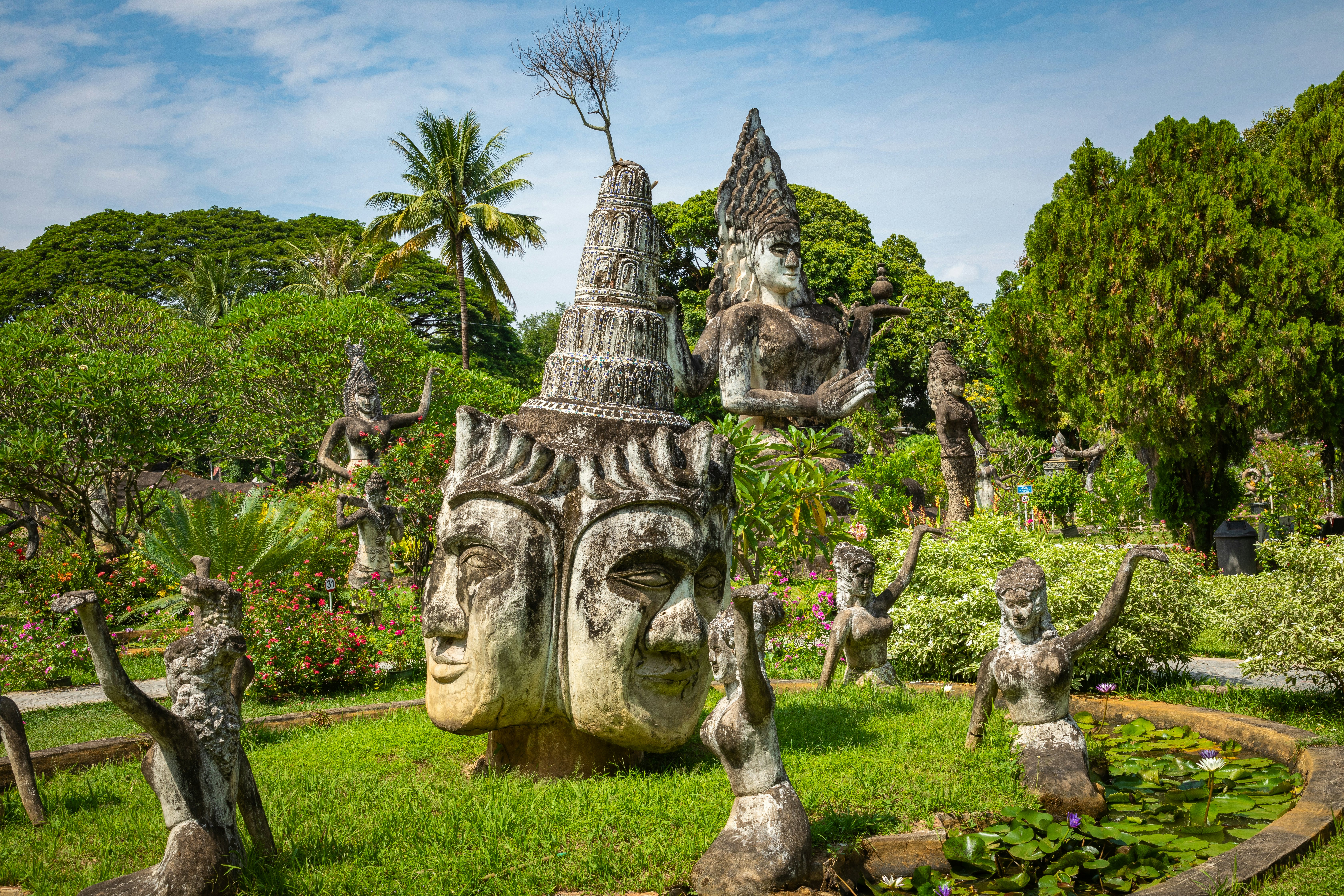 A view of sculptures of Buddhas and other deities in a tropical garden.