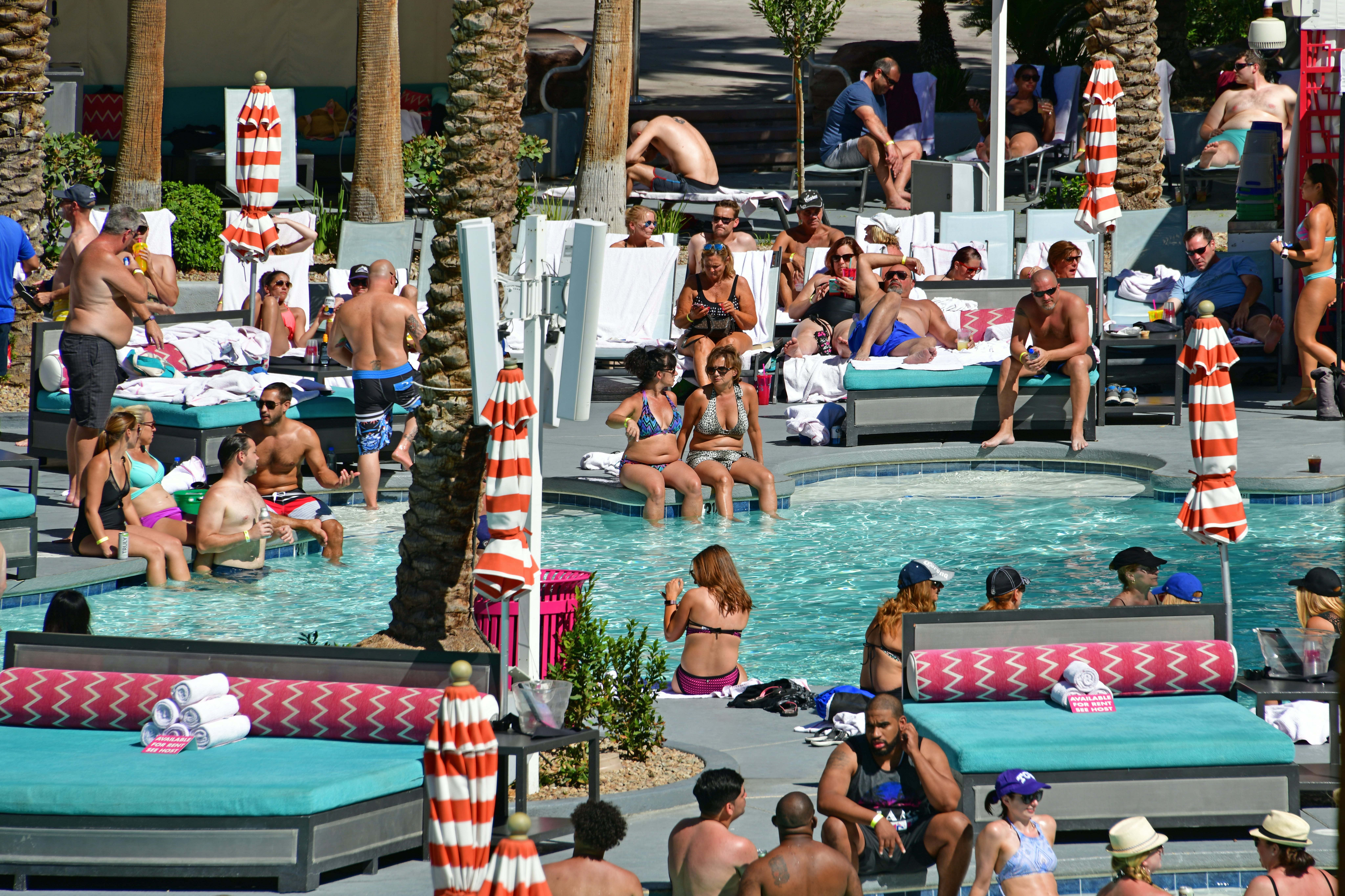 Numerous people cluster in and around a pool at a resort on a hot day.