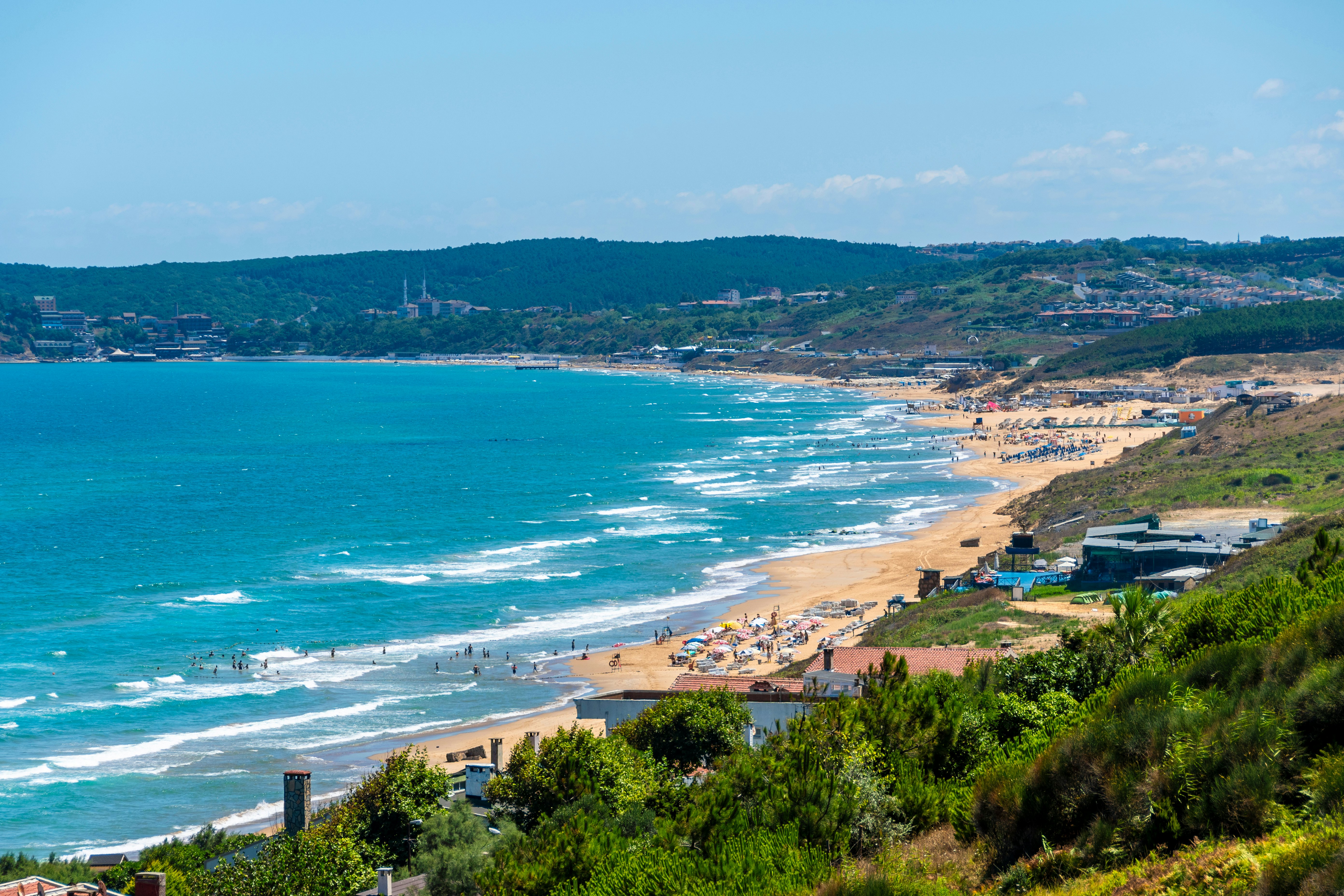 A sandy beach crowded with people on sunloungers. The surf crashes on the shore.