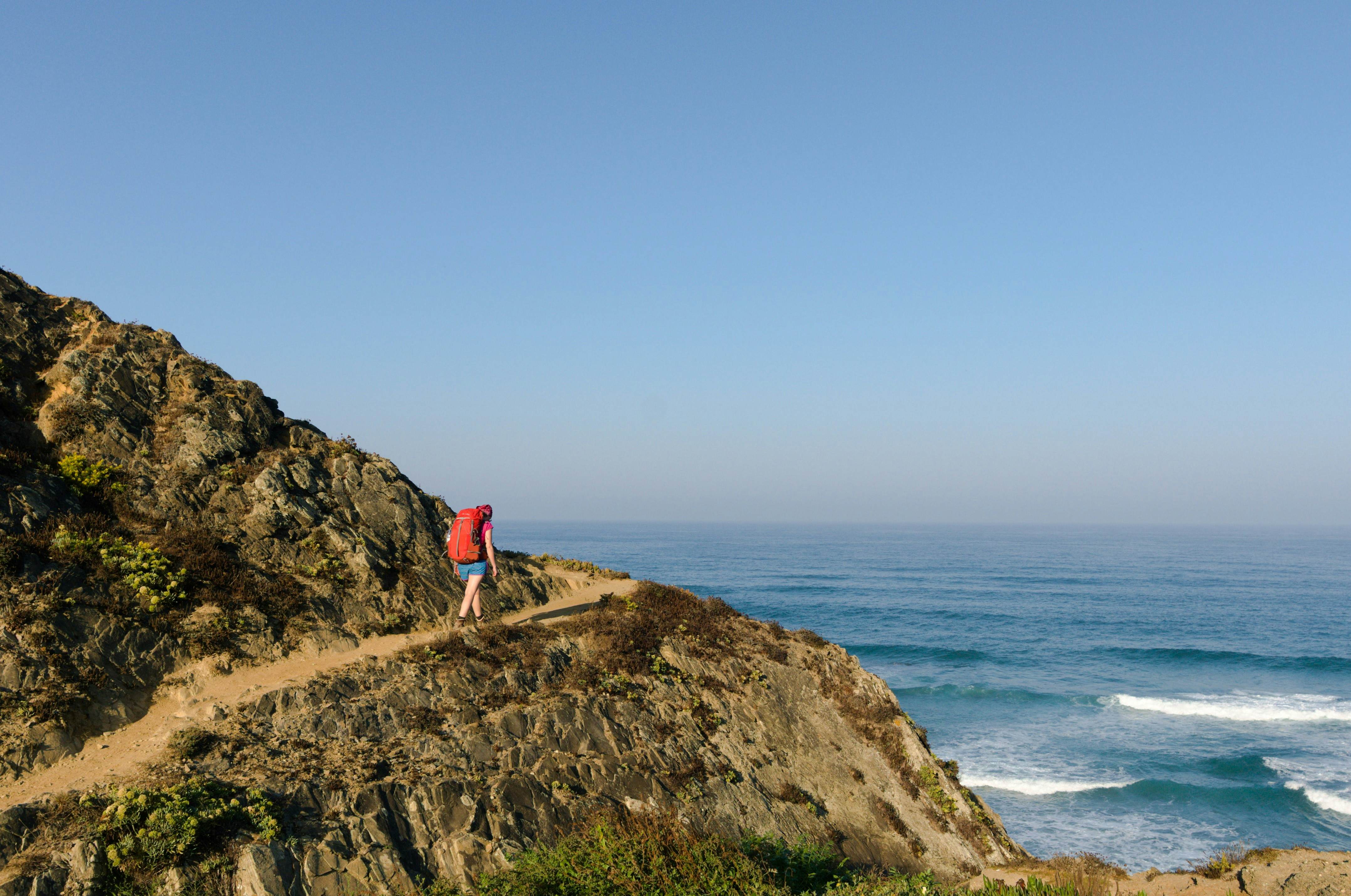 Woman with red backpack walking on the coastal trail, fishermen's trail in portugal, License Type: media, Download Time: 2026-02-23T17:37:04.000Z, User: clairenaylor, Editorial: false, purchase_order: 65050 - Digital Destinations and Articles, job: Online editorial, client: Fishermen’s Trail Portugal, other: Claire Naylor