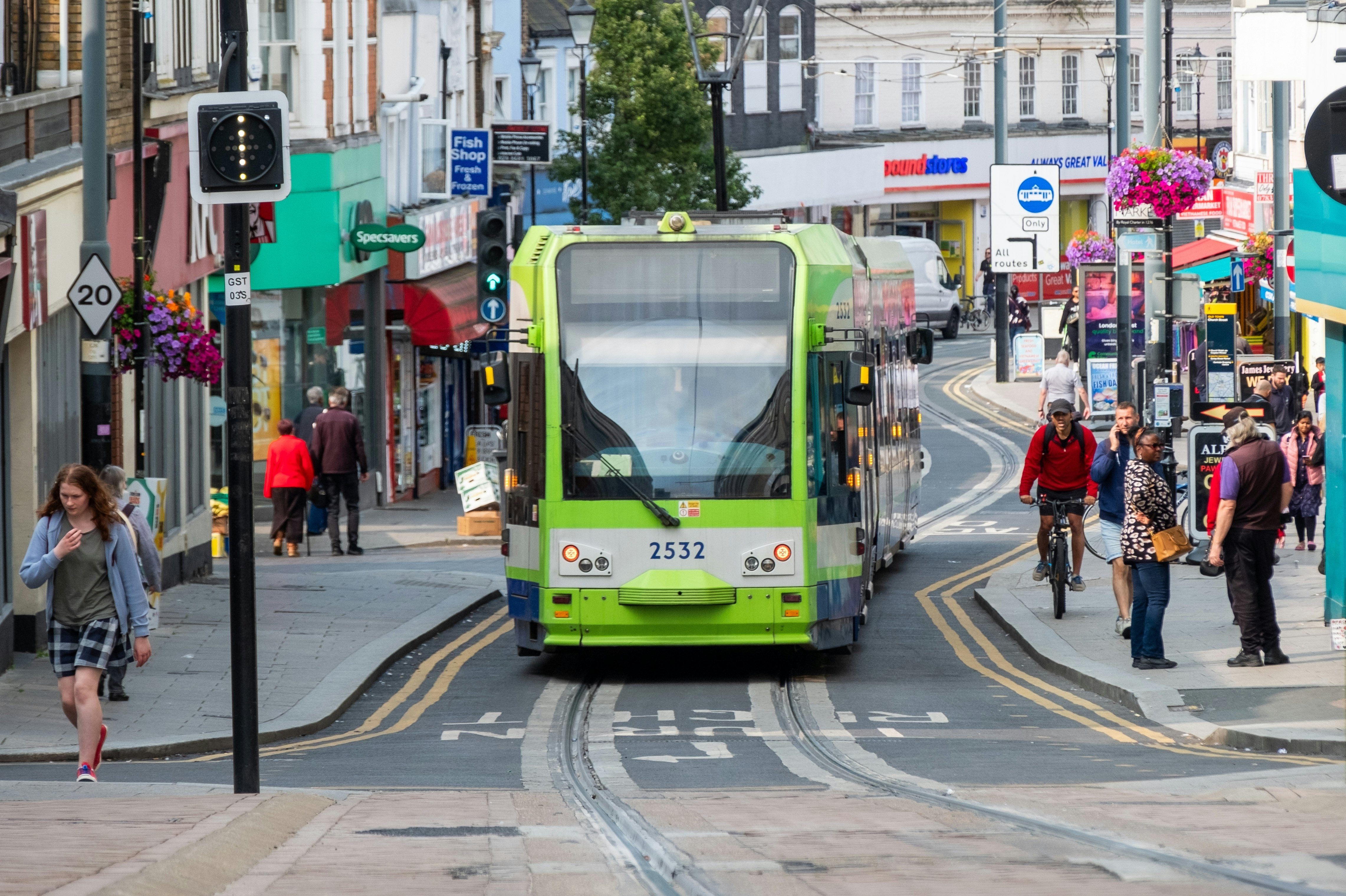 A green-painted tram is seen from the front as it winds down a busy city street.