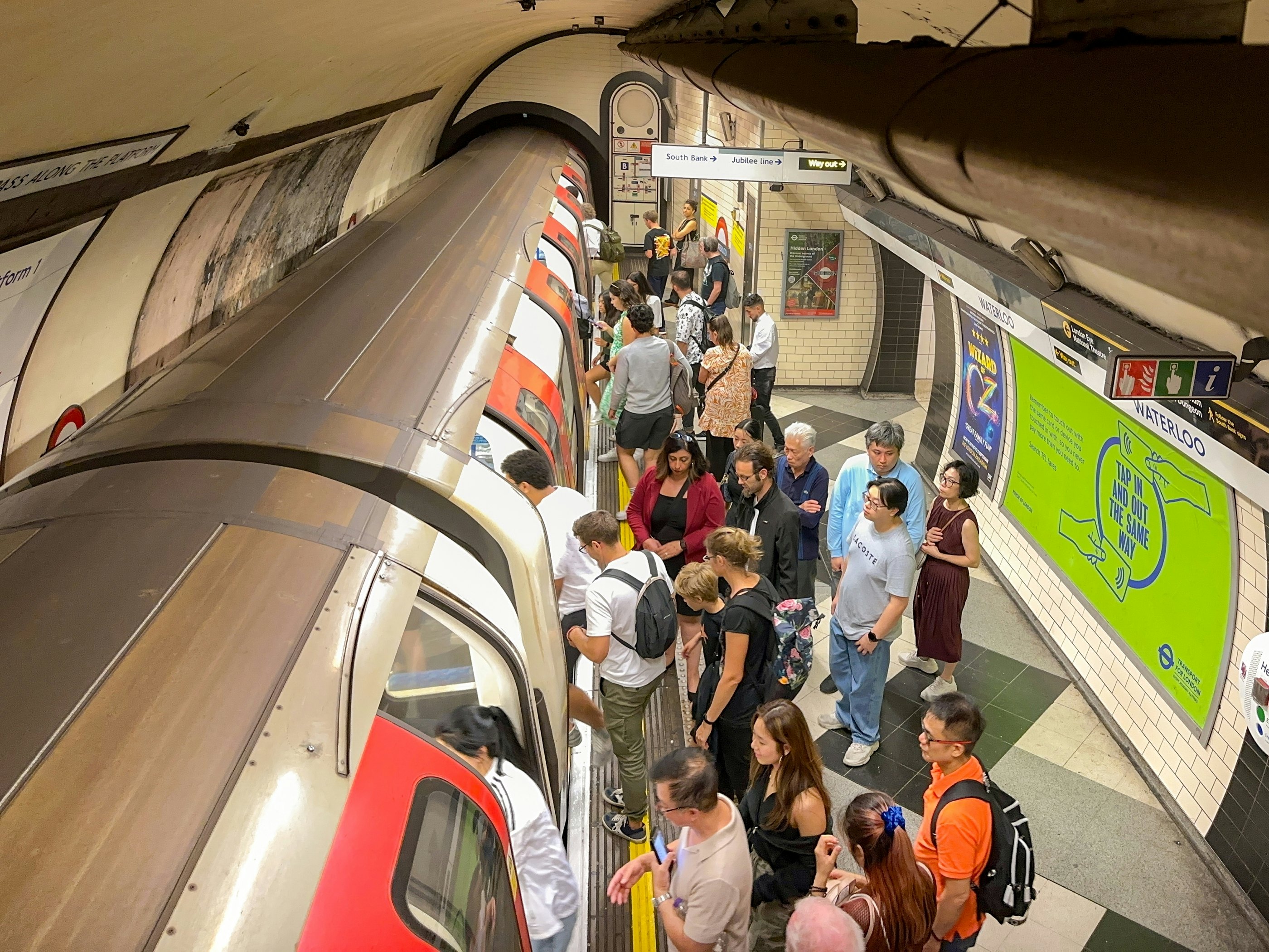 A view looking down on the platform of an underground metro station. People are gathered to board a train, which sits in the station with its doors open.