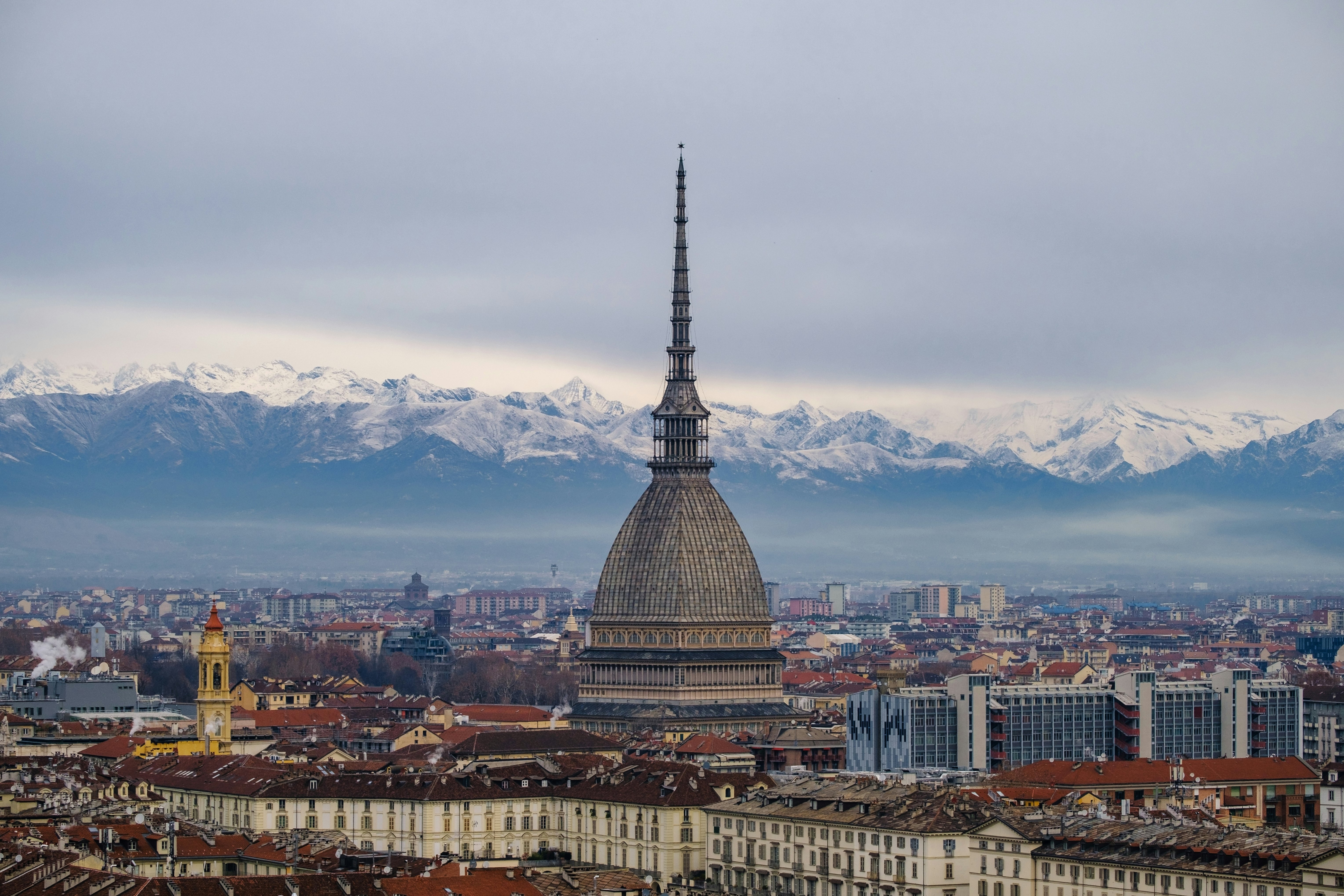 A large domed tower rises above a cityscape with snow-topped mountains in the background.