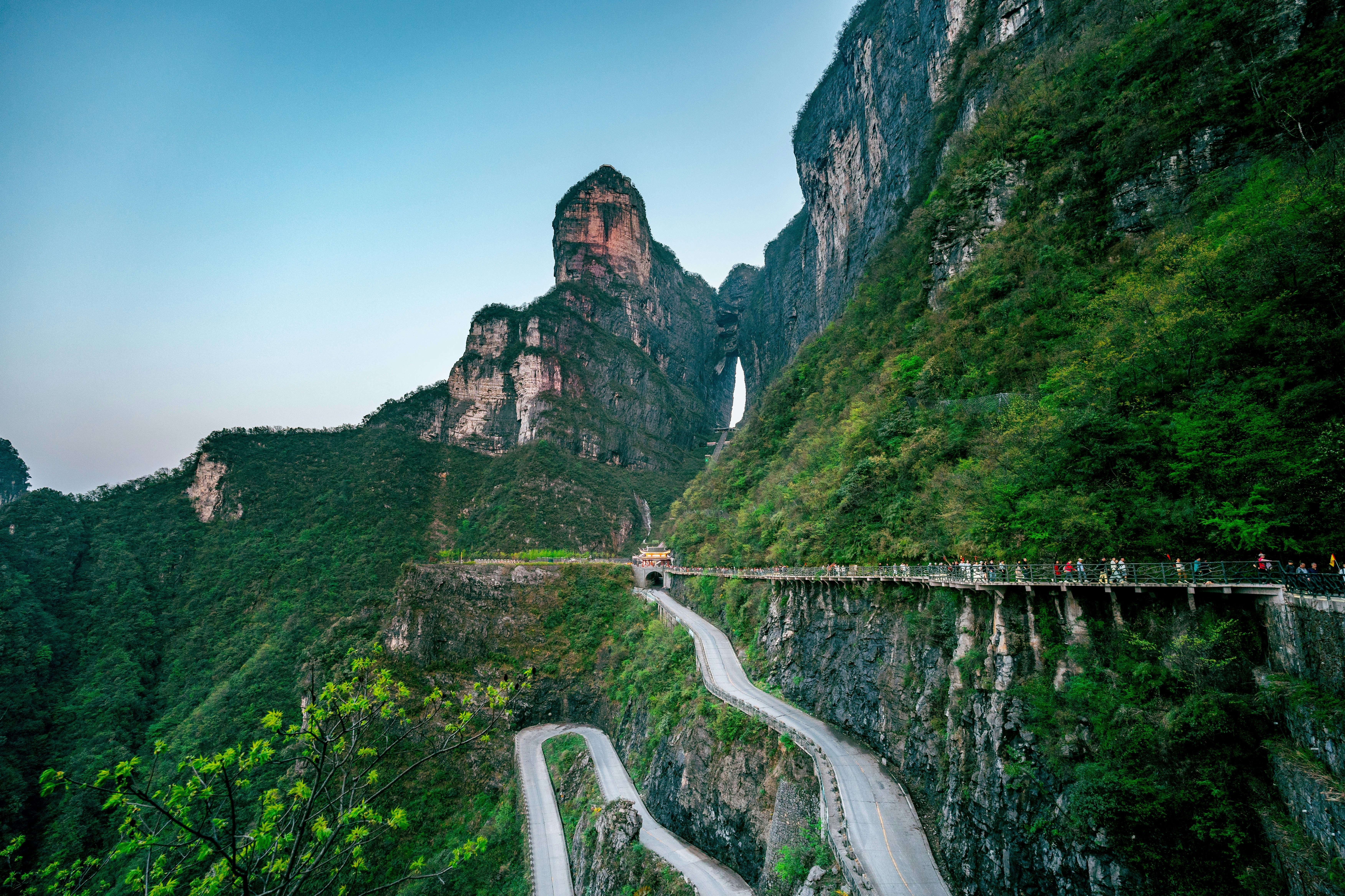 A winding paved path leads up a mountain face to high limestone peaks. A distinctive hole lets light shine through the mountain.