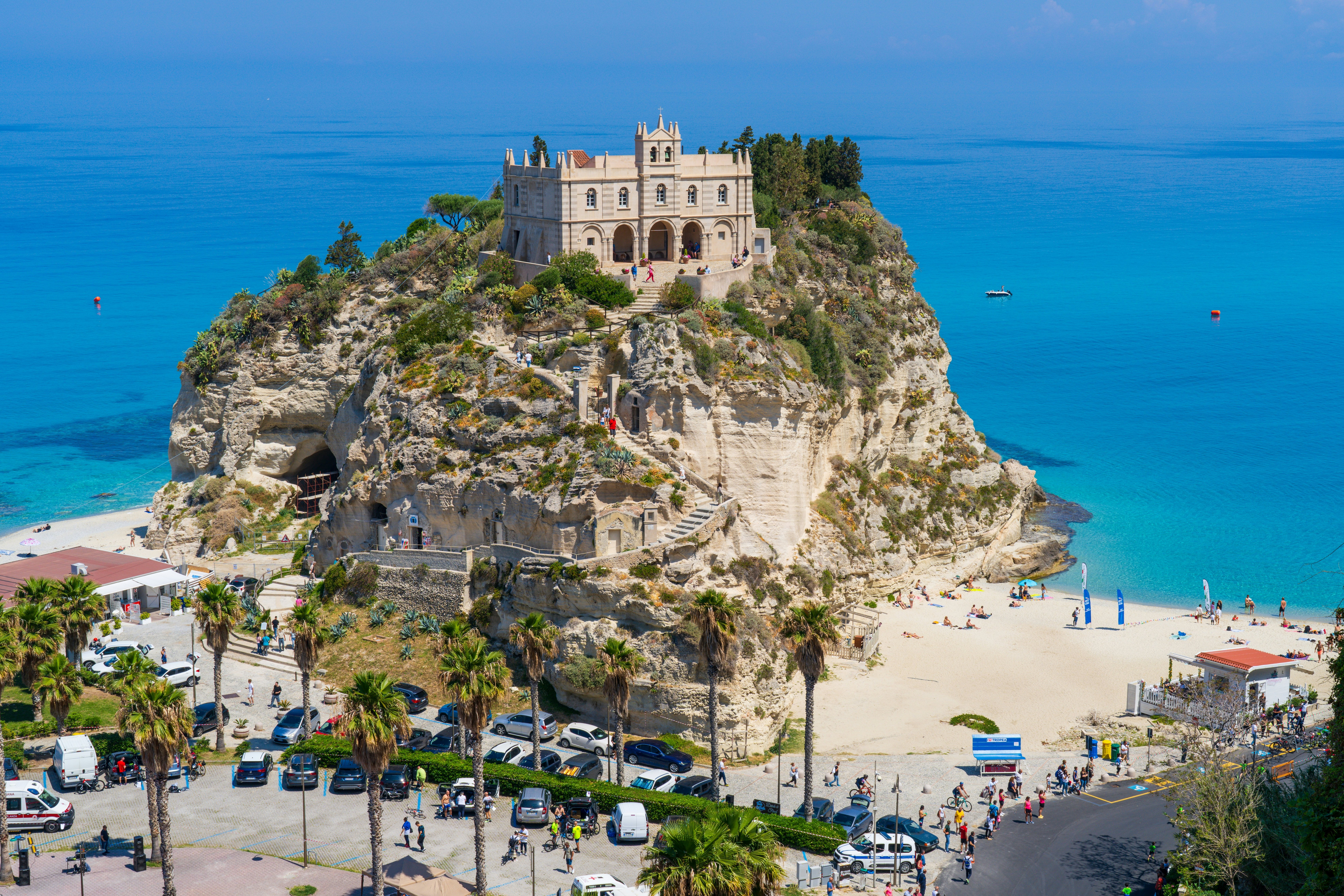 Steps weave a path around a cliff to a church. The cliff is surrounded by beautiful turquoise ocean with a sandy beach.