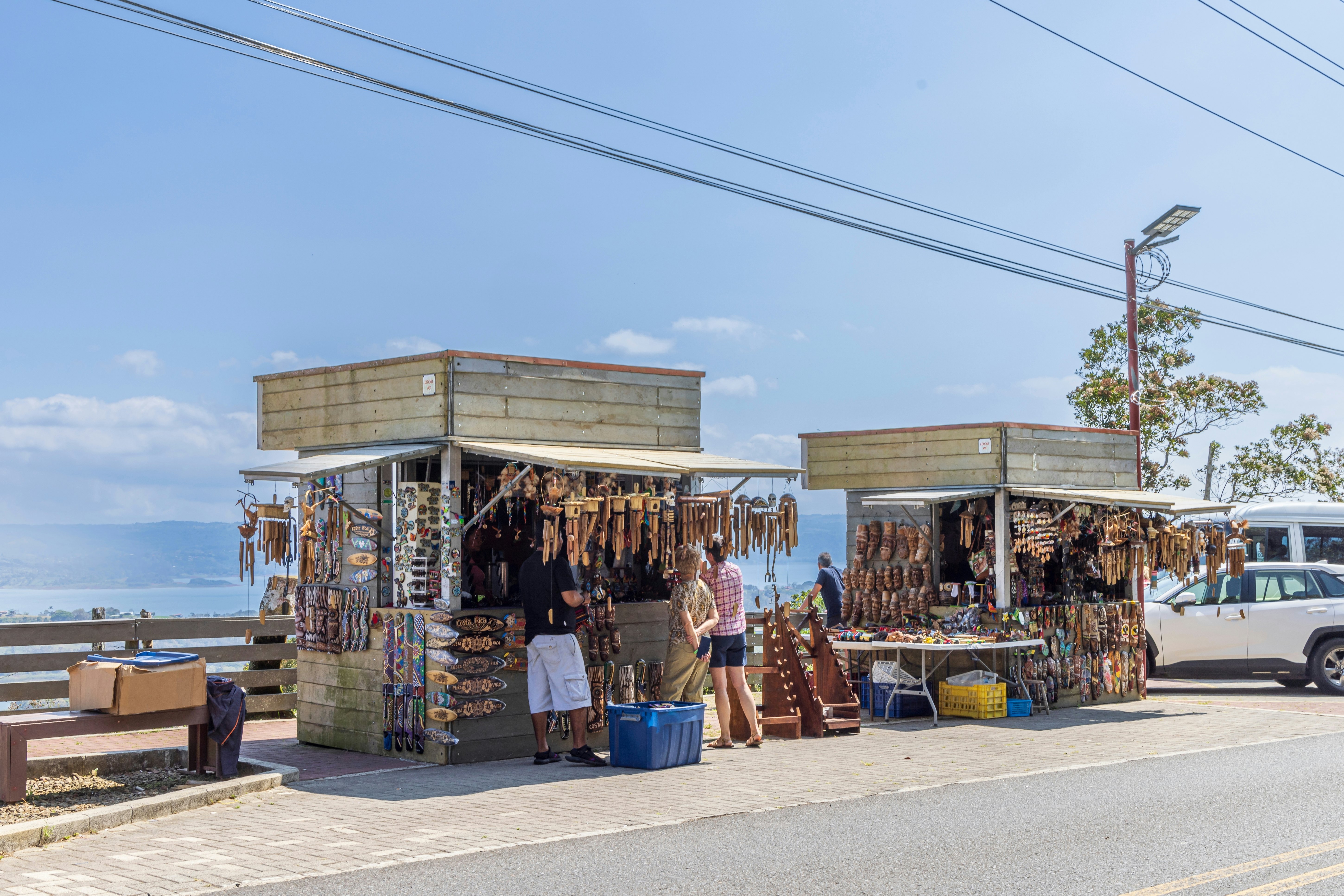A row of stalls beside a road near a lake selling wooden trinkets and souvenirs.