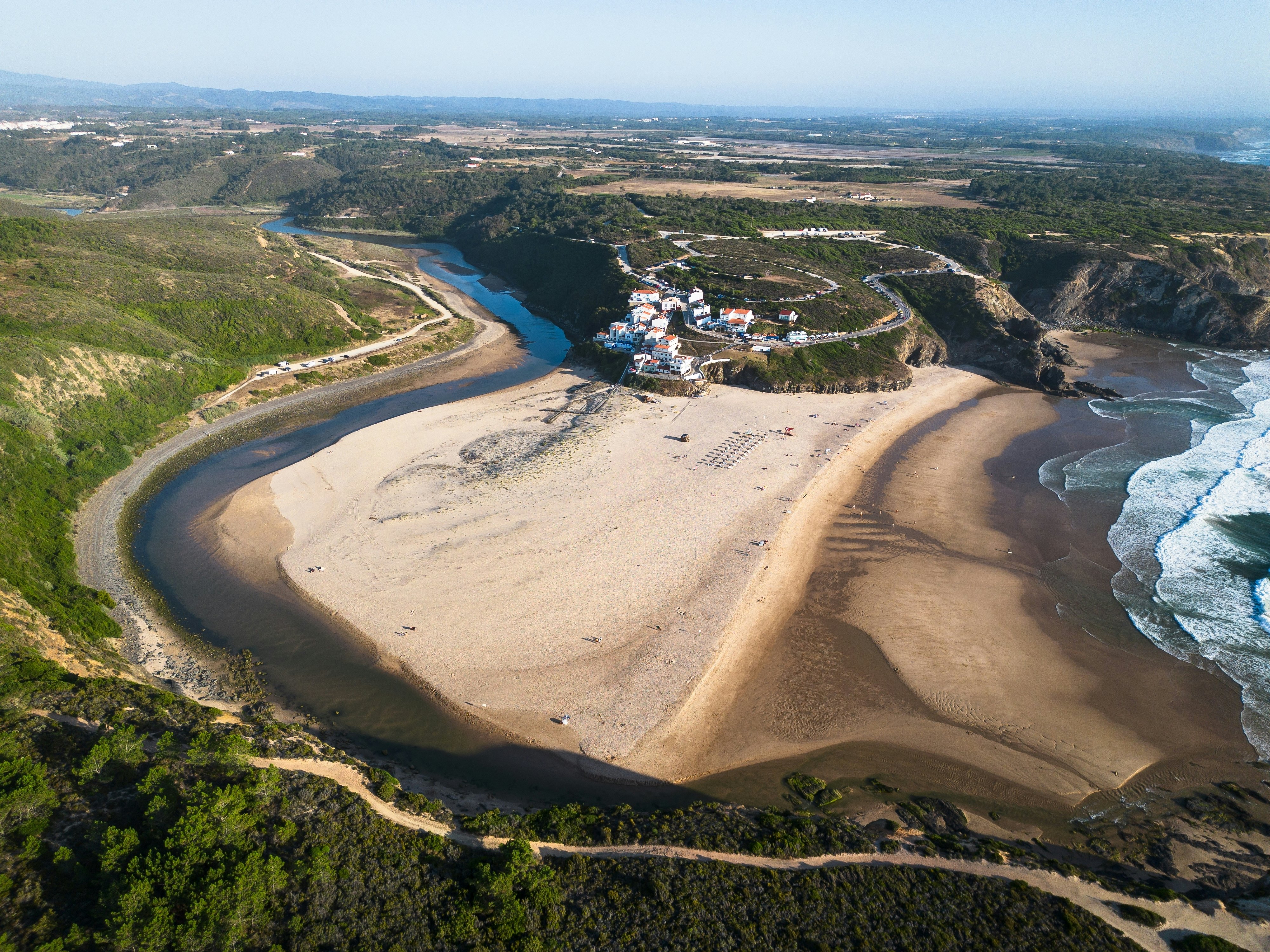 An aerial shot of a beach formed by the oxbow of a river reaching the sea.