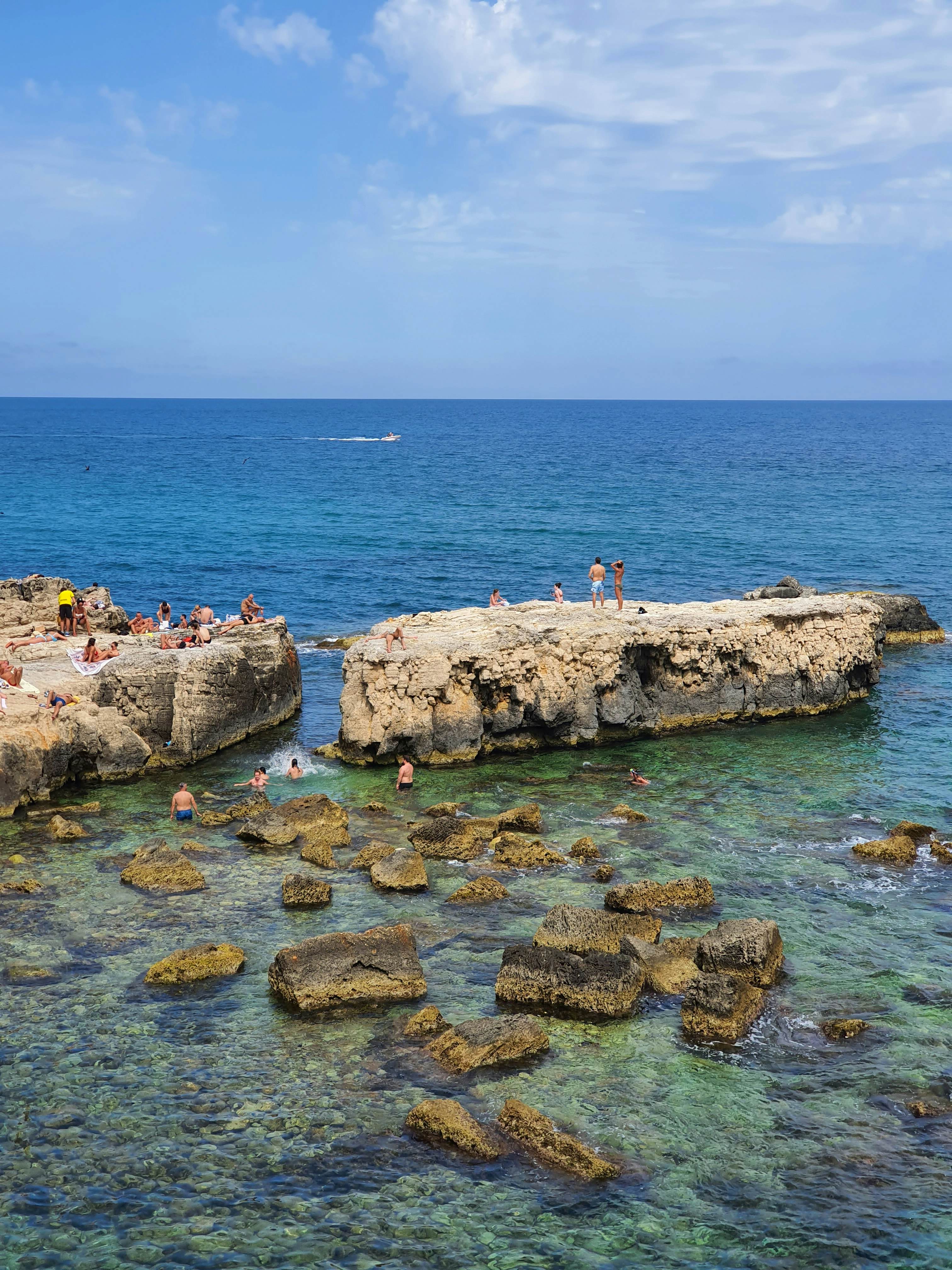 Swimmers stand on high rocks and swim in the ocean.