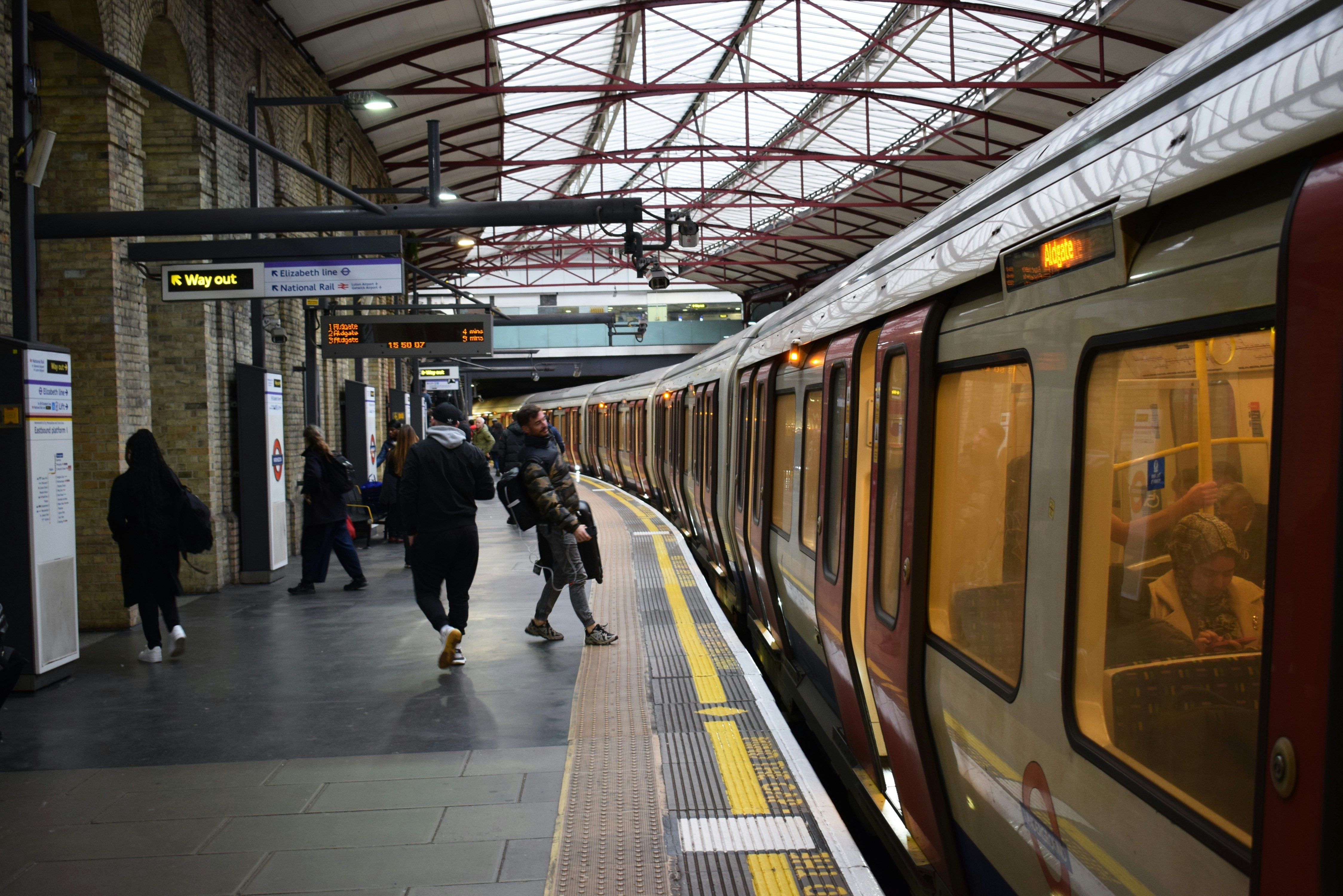 People stand on the platform as a train pulls into a station, covered by skylights.
