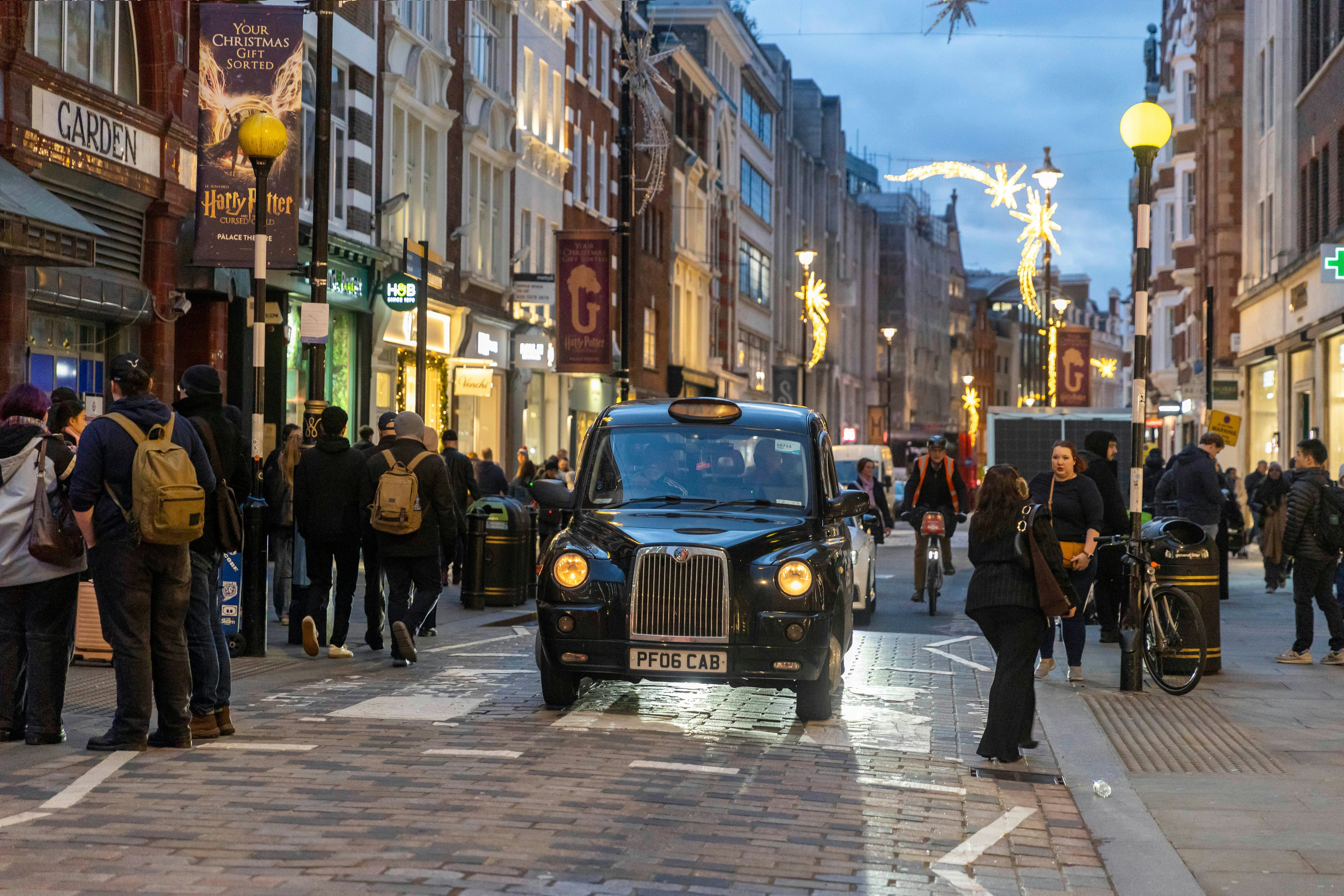 A black taxi drives down a busy city street at dusk.