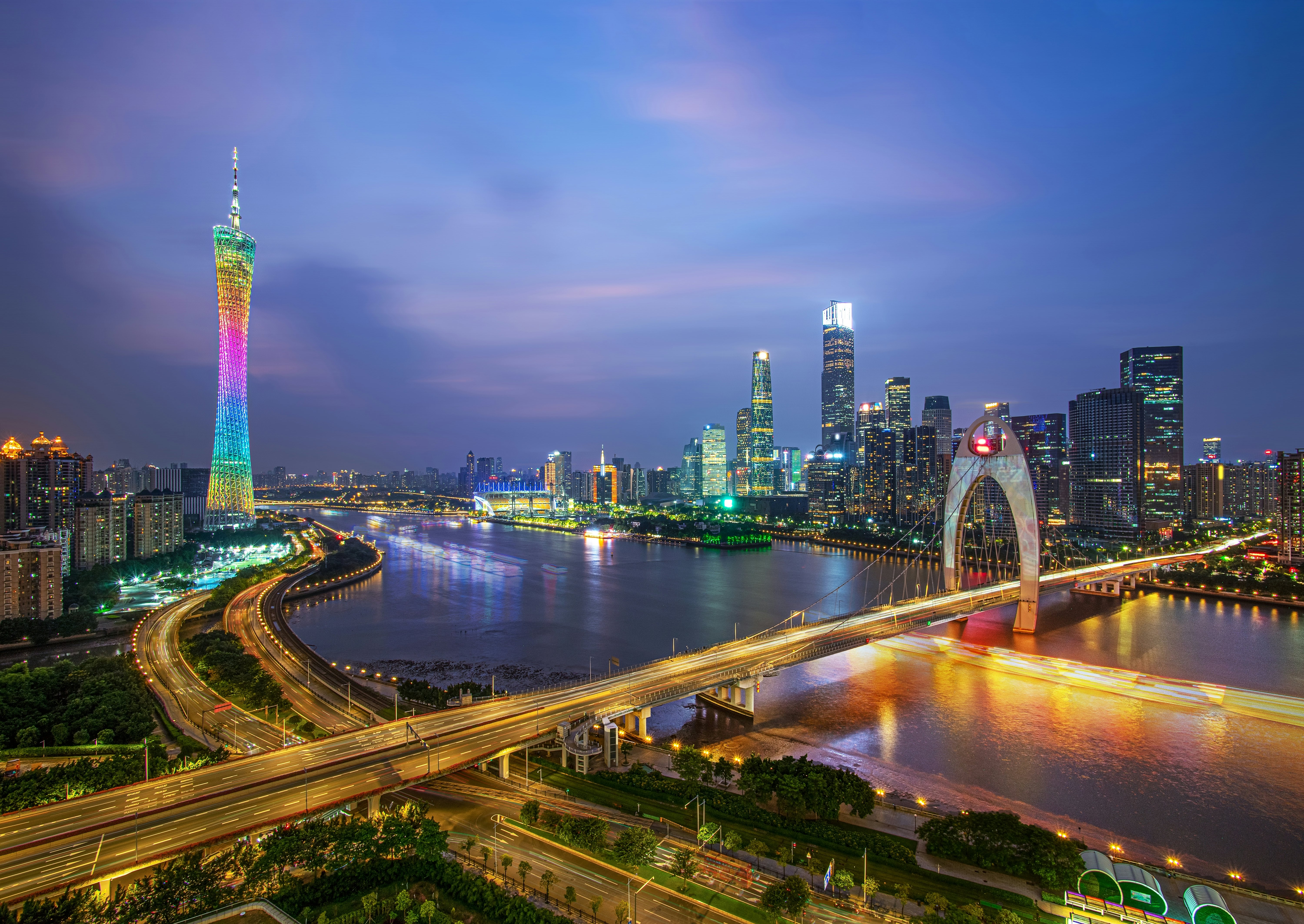 Night in a high-rise city with bridges, roadways and buildings lit up in bright lights and neon.