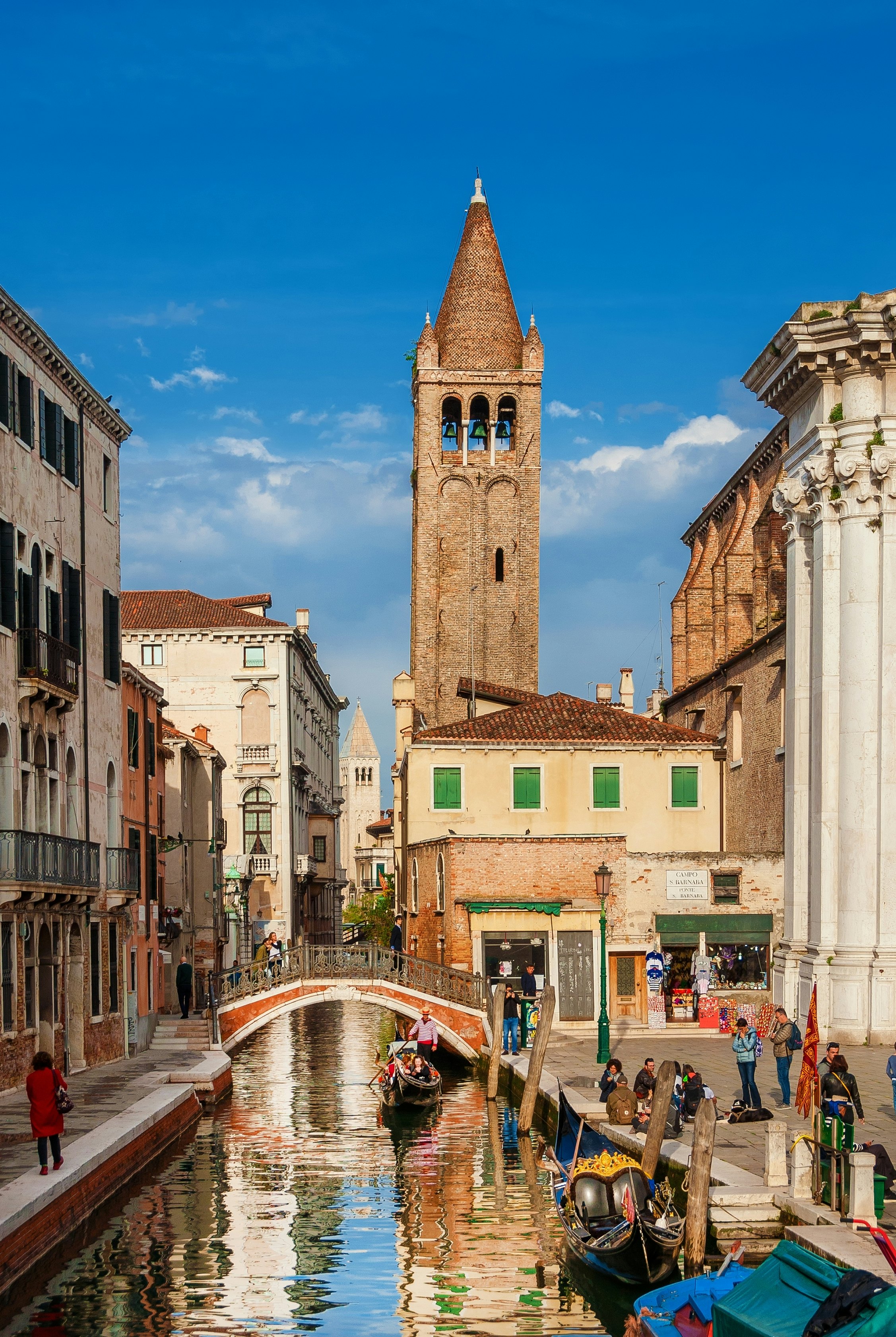 VENICE, ITALY - APRIL 26, 2019: Tourism in Venice. View of Rio San Barnaba canal with gondolas, old bell tower and tourists in Dorsoduro historic district,
