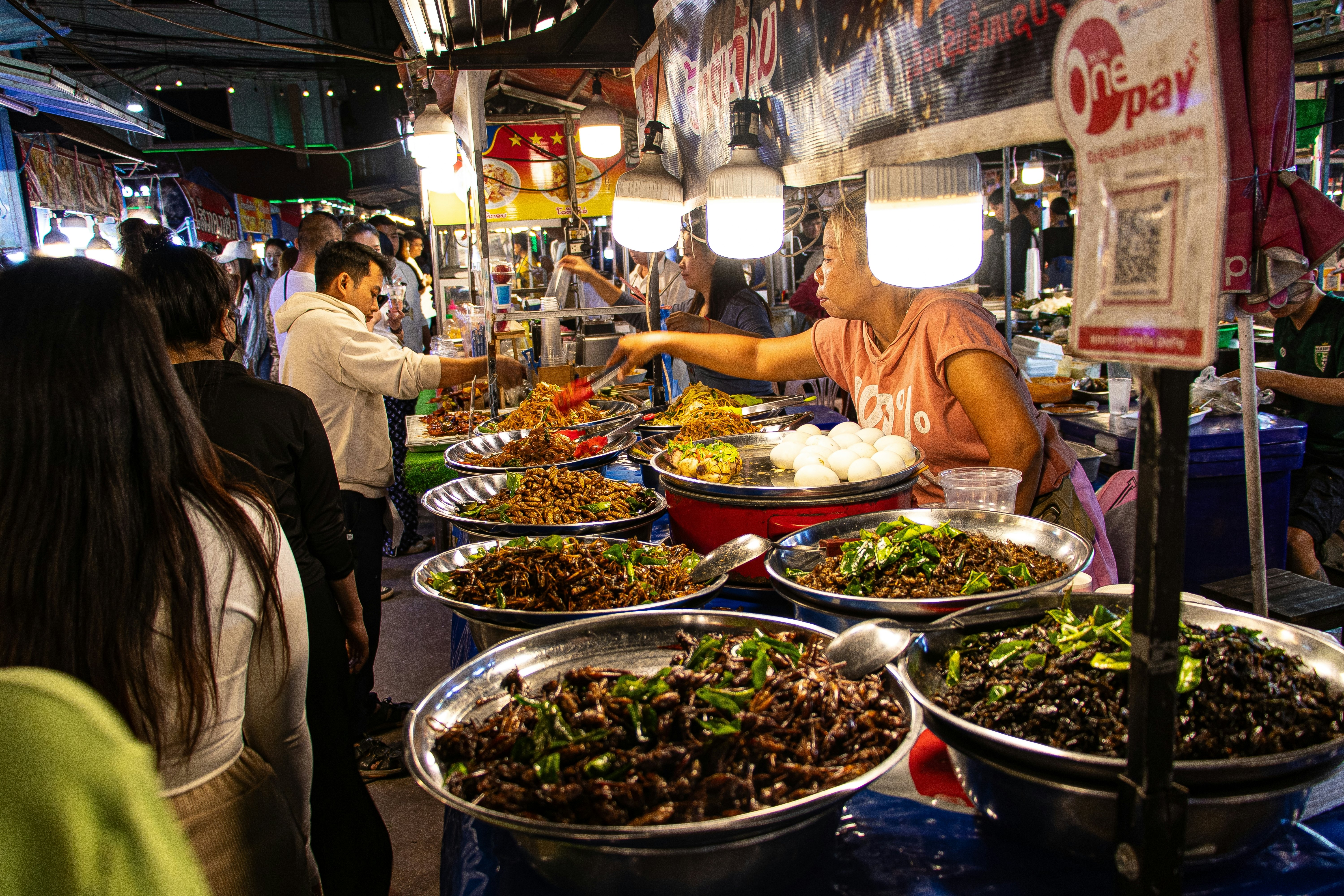 A vendor prepares different types of food at a stall at a night market in a city.