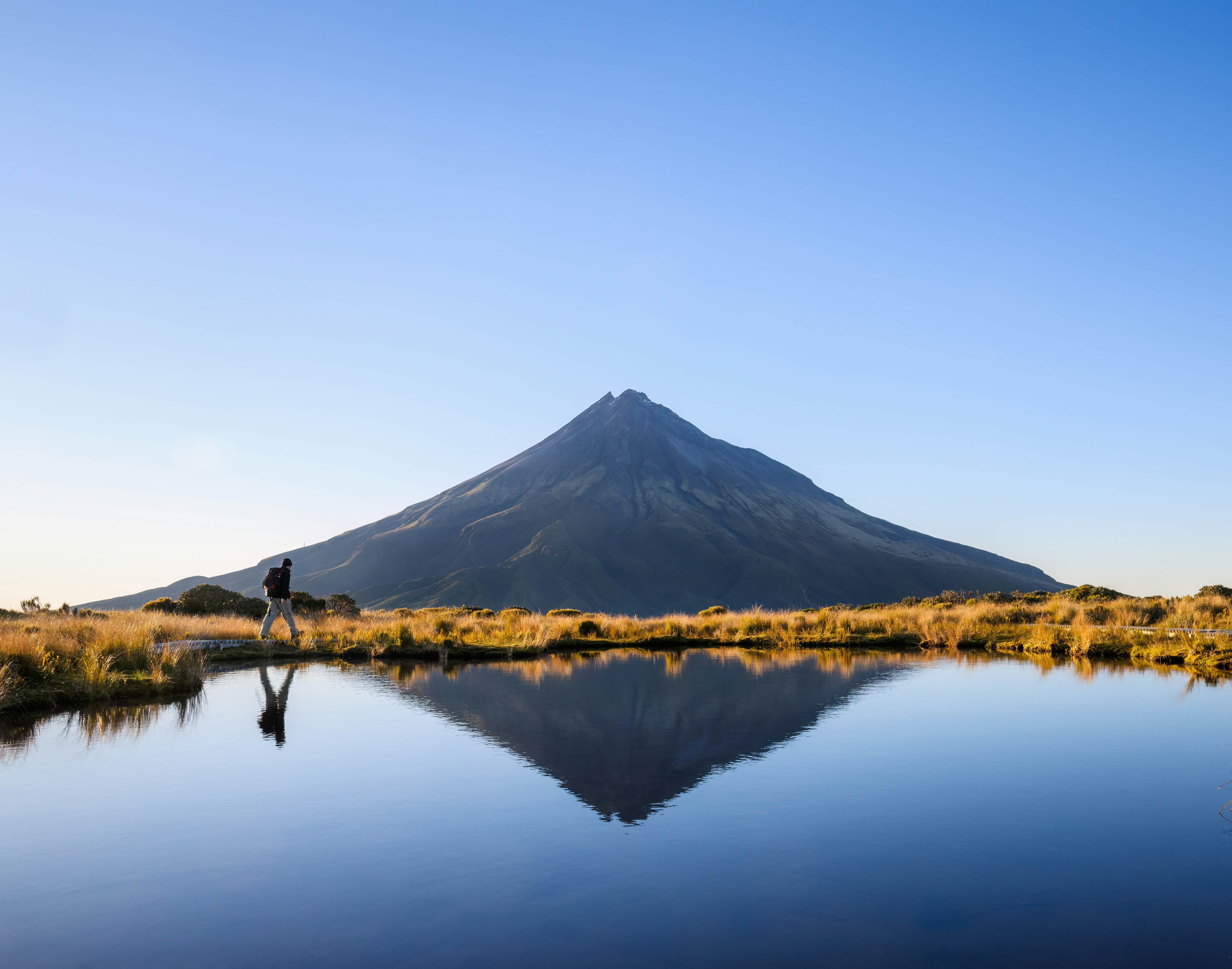 Man hiking the Pouakai circuit. Mt Taranaki under the clear blue sky. New Zealand., License Type: media, Download Time: 2025-02-11T21:07:08.000Z, User: Ppeterson948, Editorial: false, purchase_order: 56530 - Guidebooks, job: Global Publishing WIP, client: Global Publishing WIP, other: Pia Peterson Haggarty