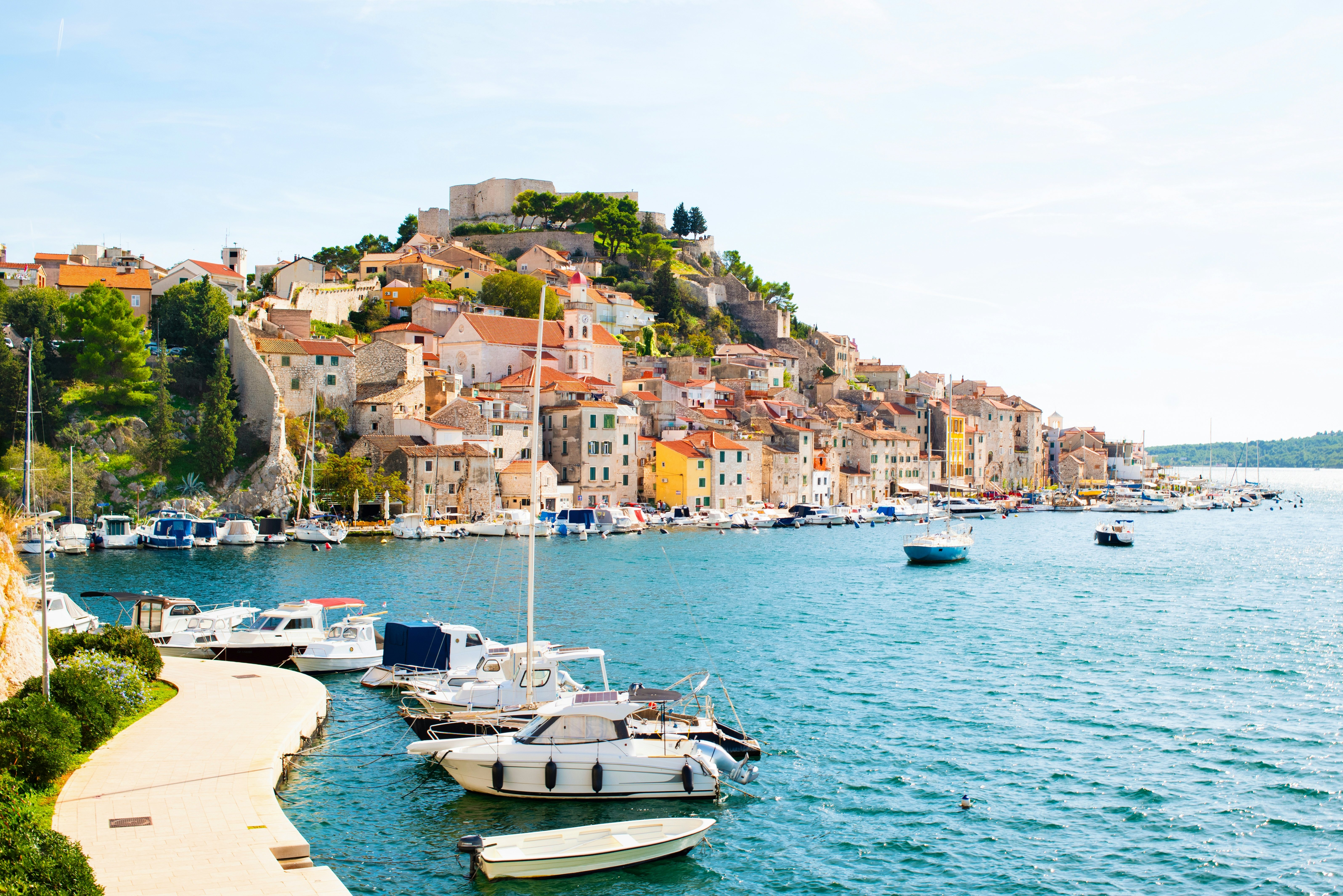 Small boats docked around the edge of a harbor with a town built into the steep hillside.