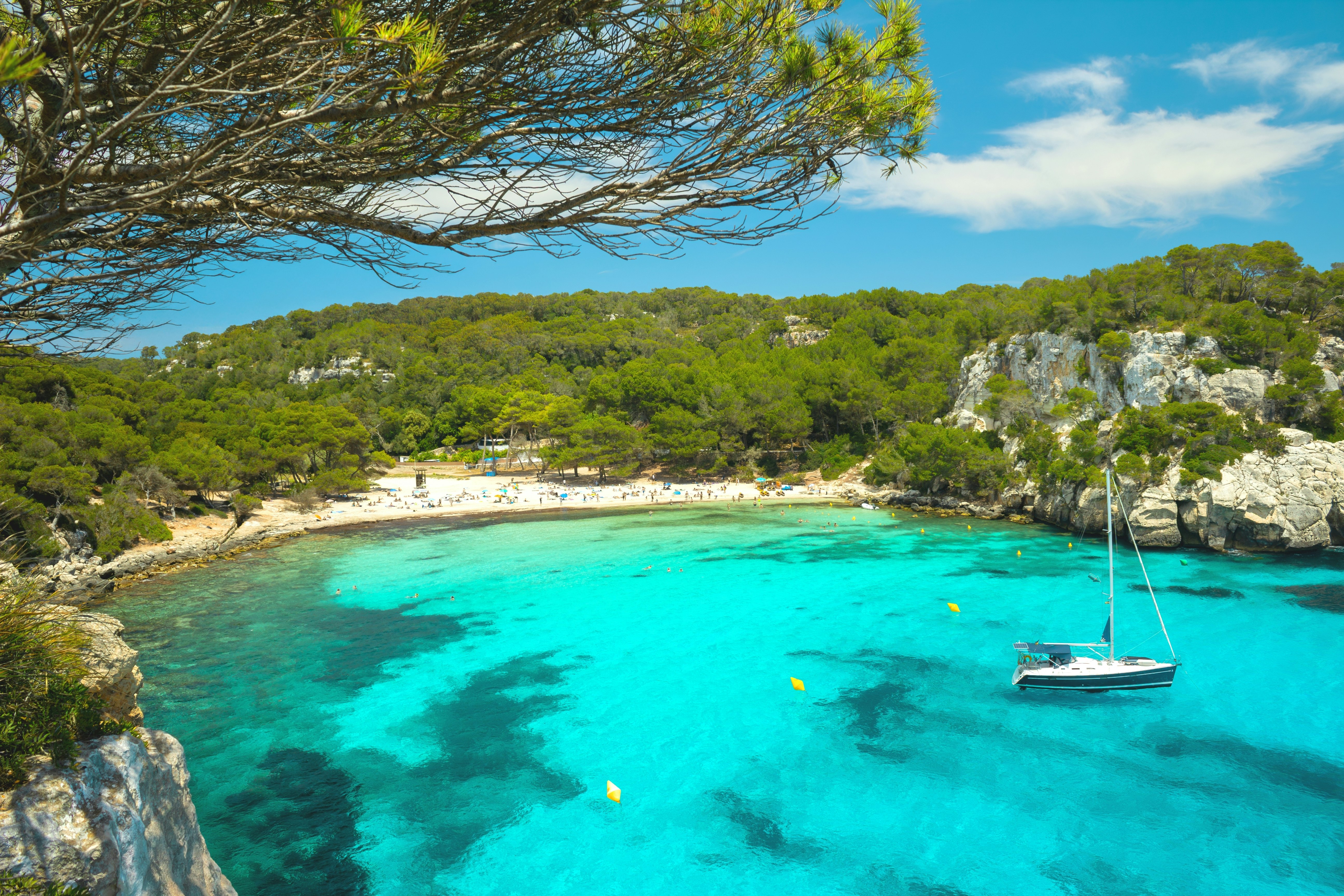 A tiny bay tucked between cliffs. People fill the small beach and splash in the turquoise waters.