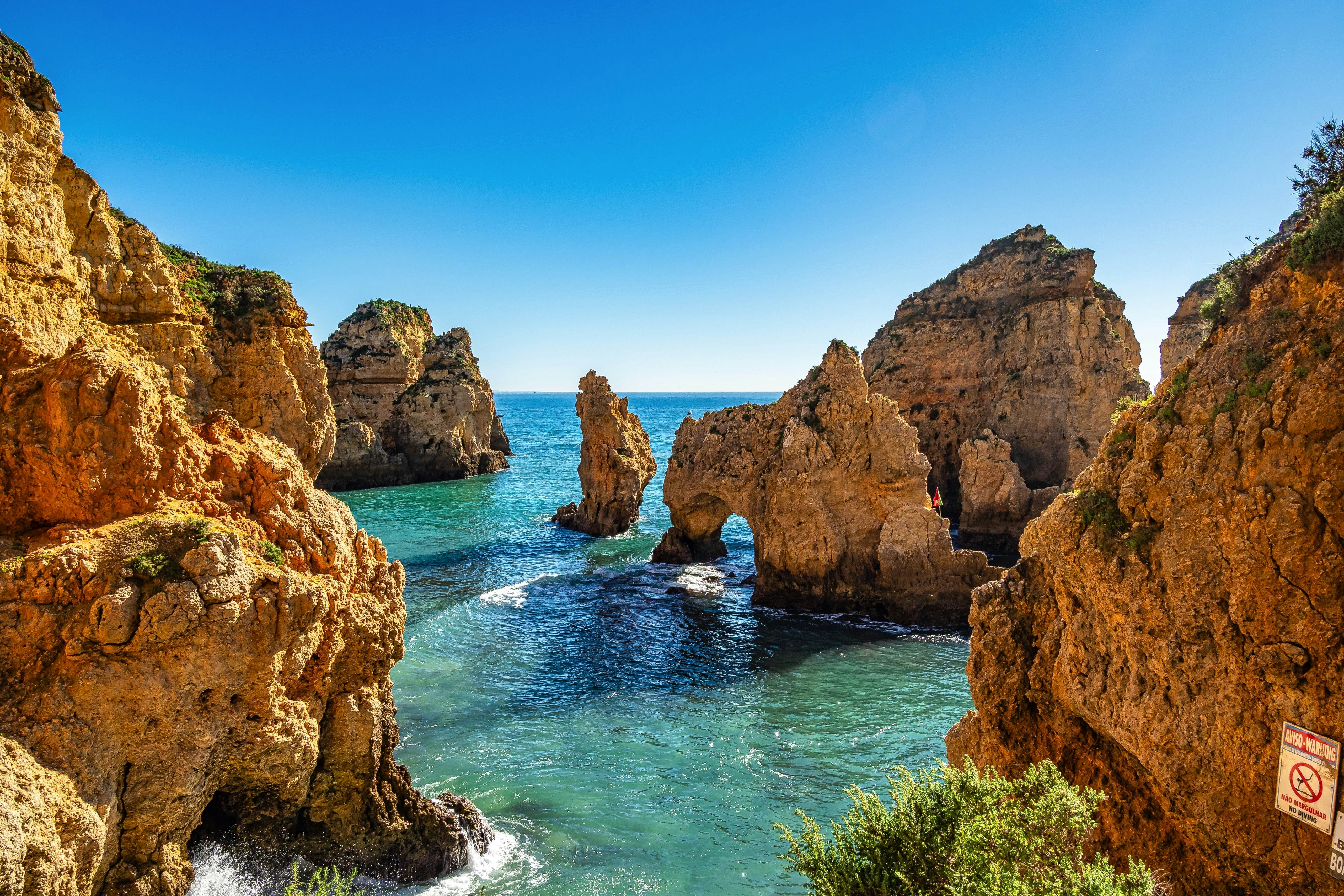A series of rock sea arches and stacks lapped by ocean waves in the sunshine.
