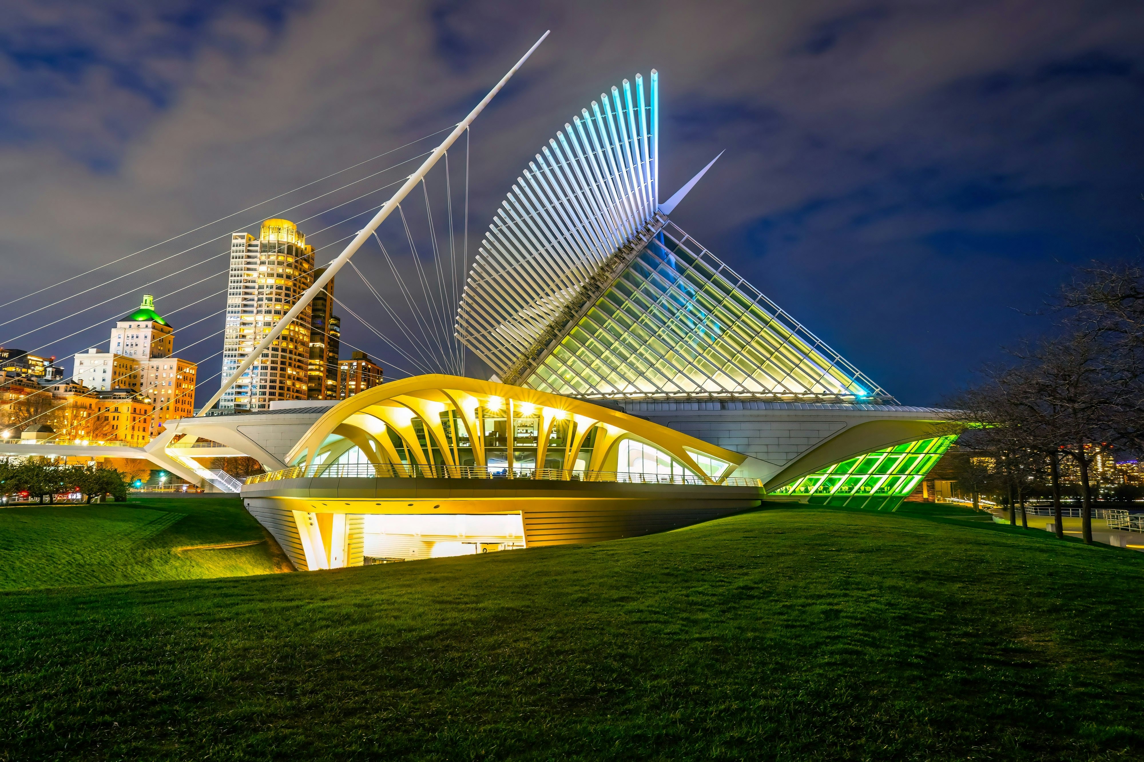 A strikingly modern pavilion of a museum, with “fins” and glass walls, is illuminated by night in a city park.