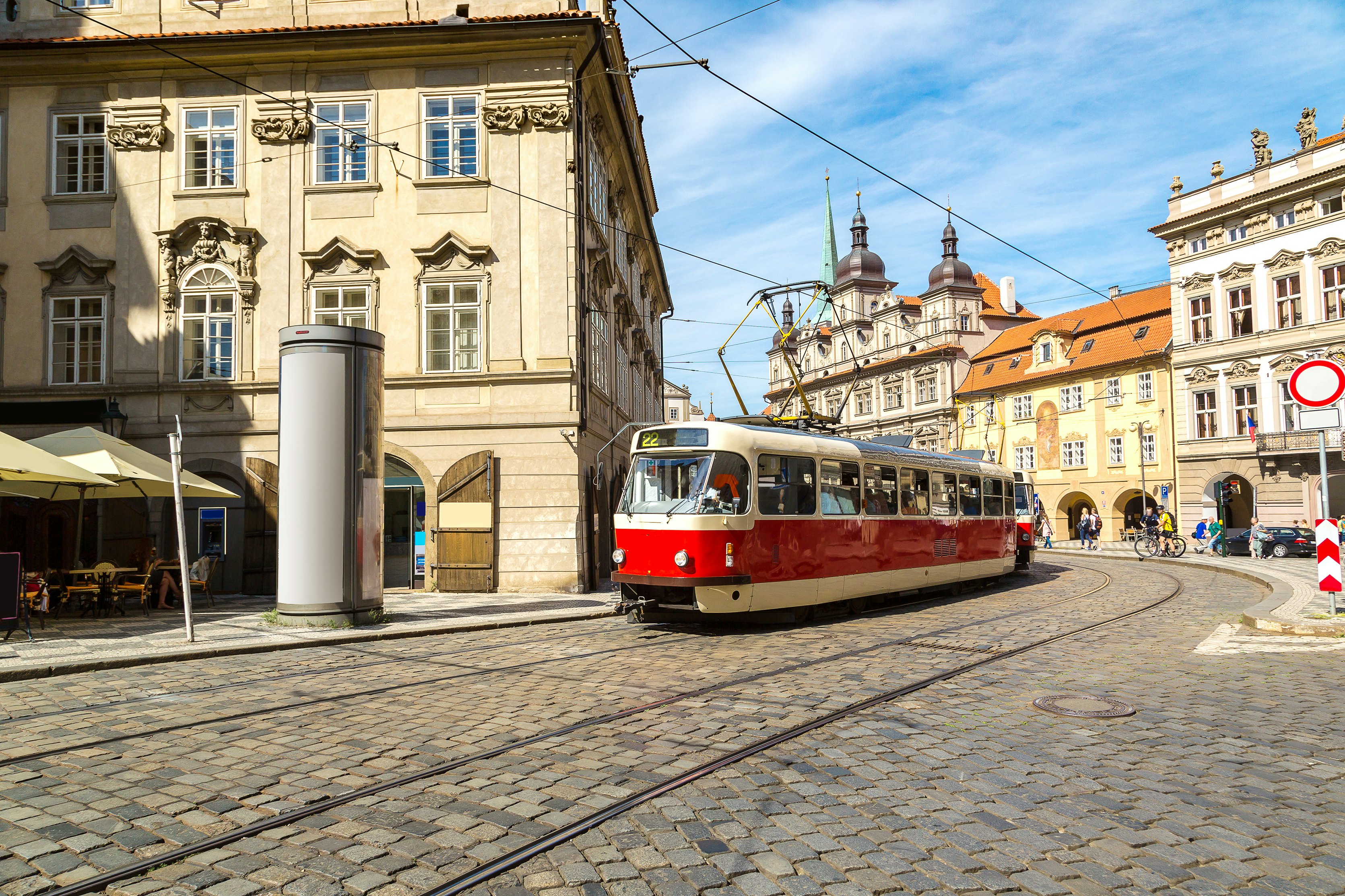 A vintage-style tram runs along a cobbled street in Prague on a sunny summer day, Czechia.