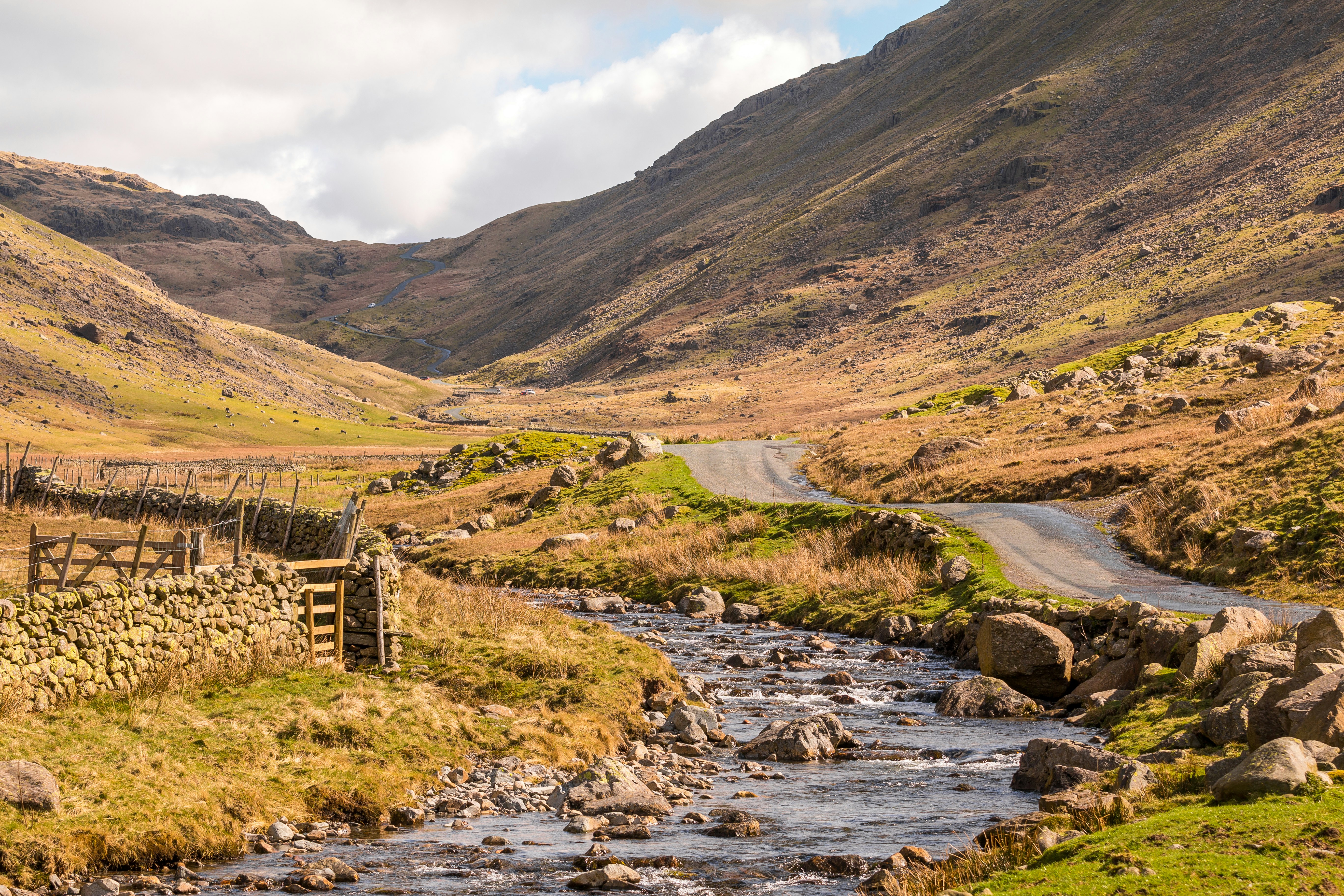 A view of a stream and country road in an empty landscape at Wrynose Pass, Cumbria, England.