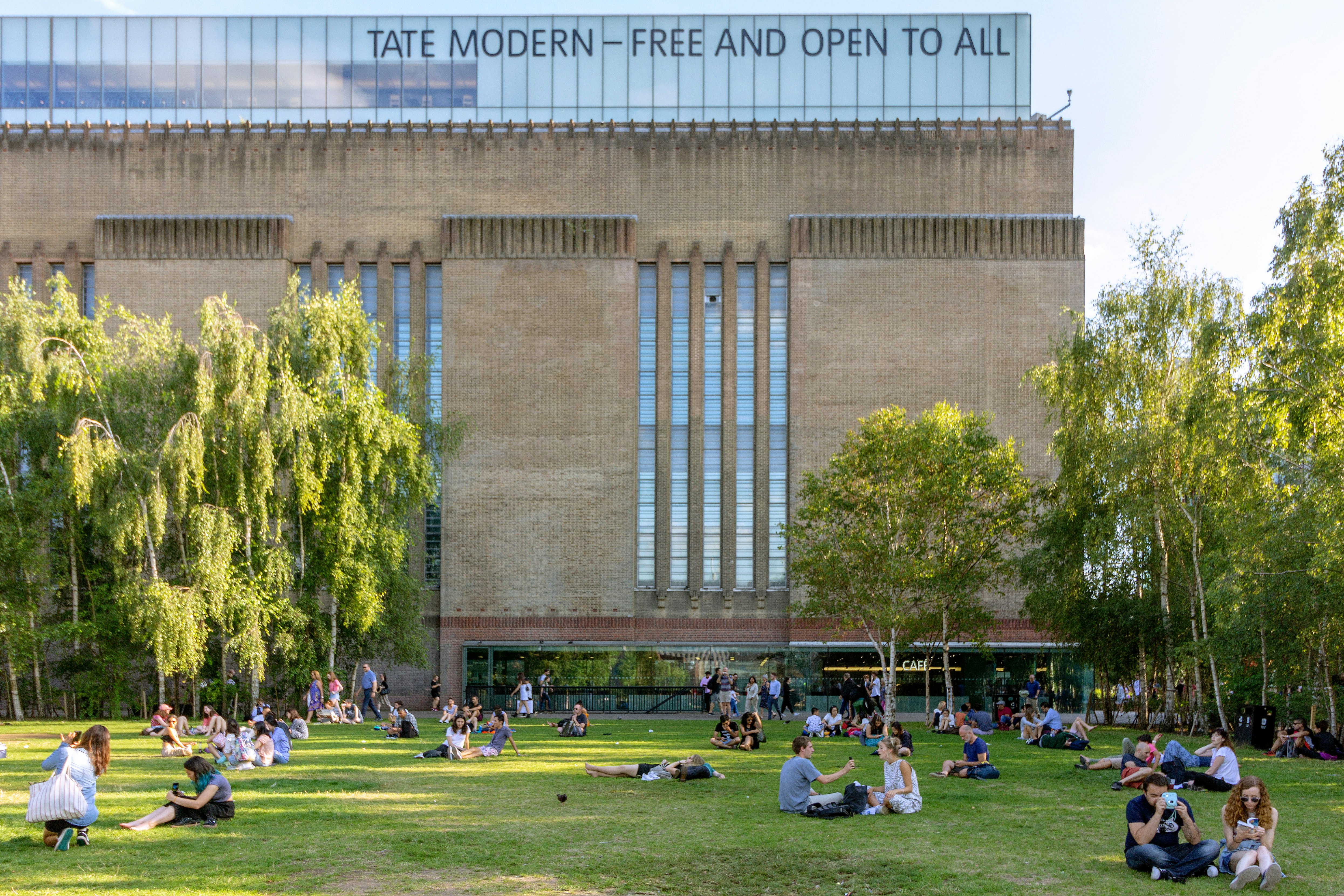 AUGUST 2, 2018: People seated on the grass outside the Tate Modern art gallery.