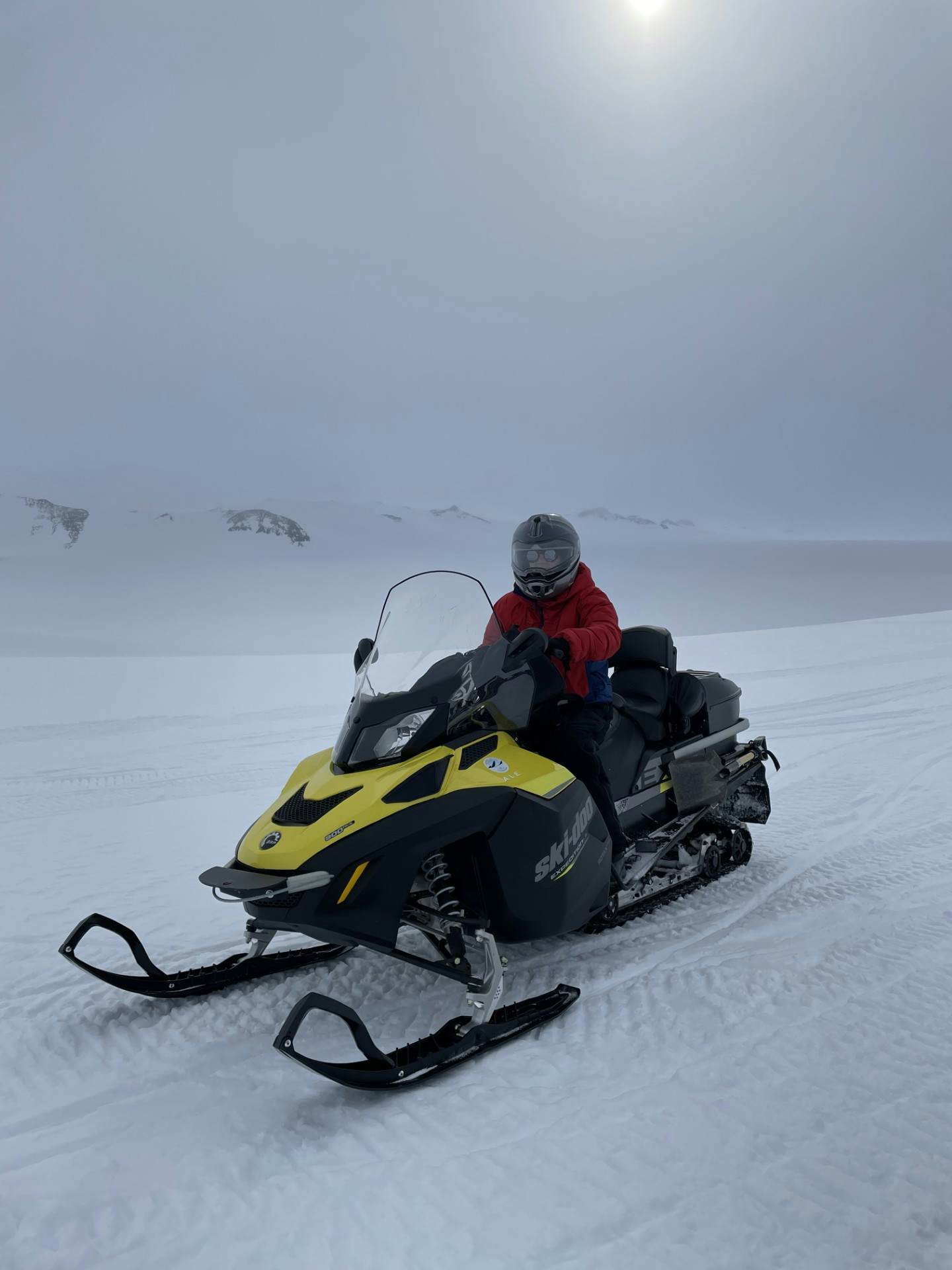A person in cold-weather gear on a yellow and black snowmobile