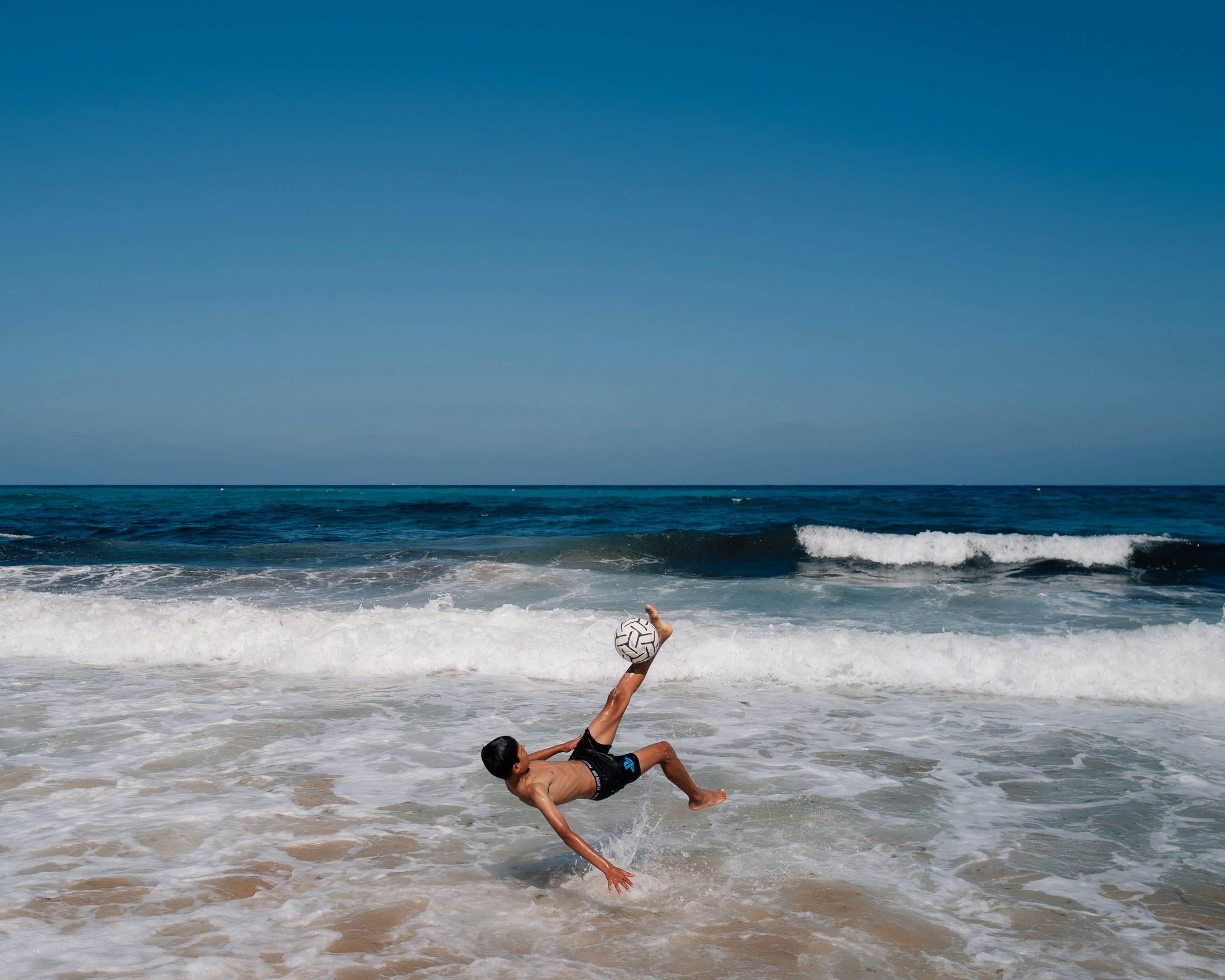 A young boy attempts a bicycle kick in the surf on a beach in Tangier, Morocco.