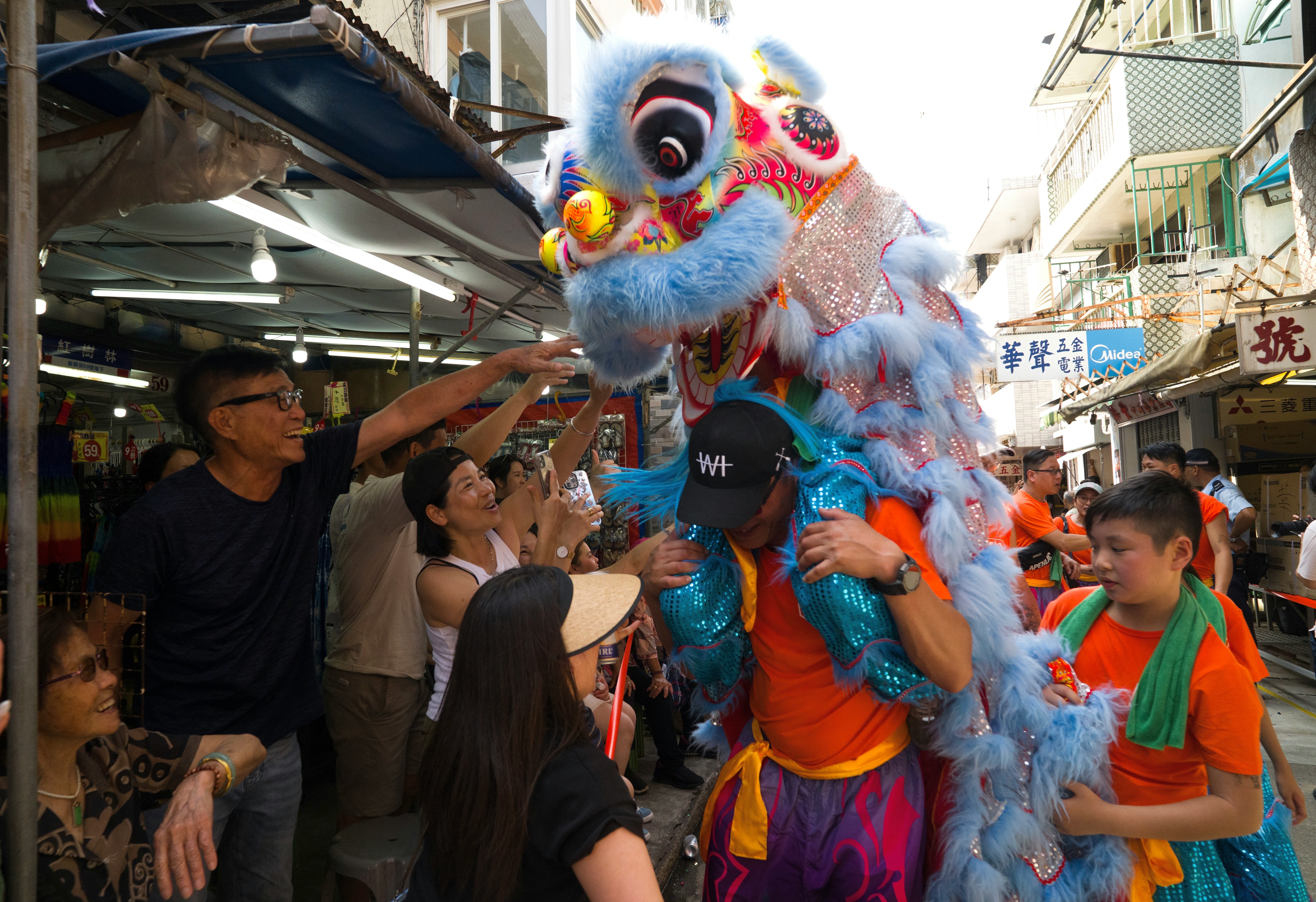 People gather around a man wearing a dragon costume during a parade in a narrow street in a town.