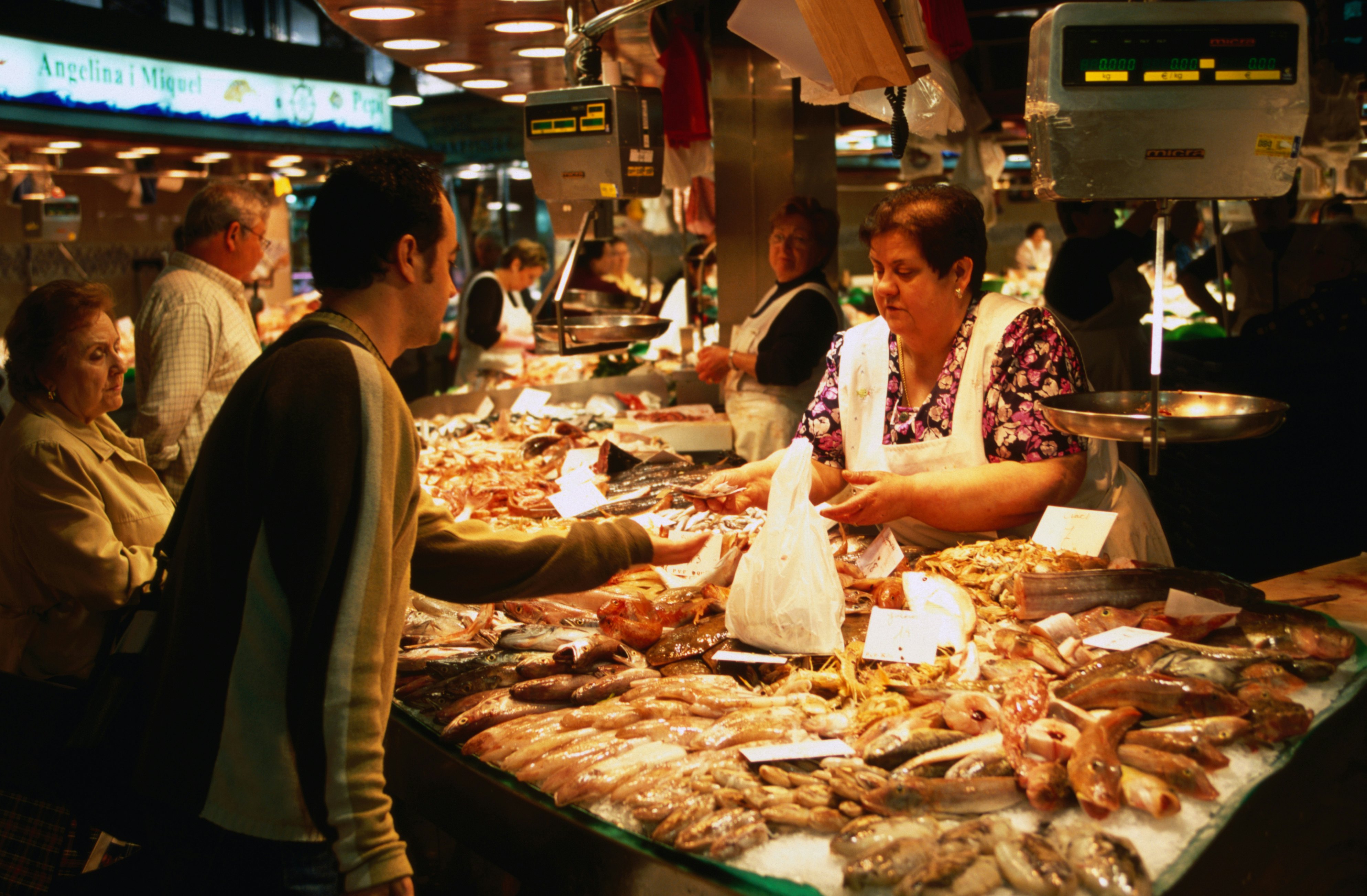 A shopper gets change from a vendor at a fish stand that has many varieties of seafood displayed on ice.