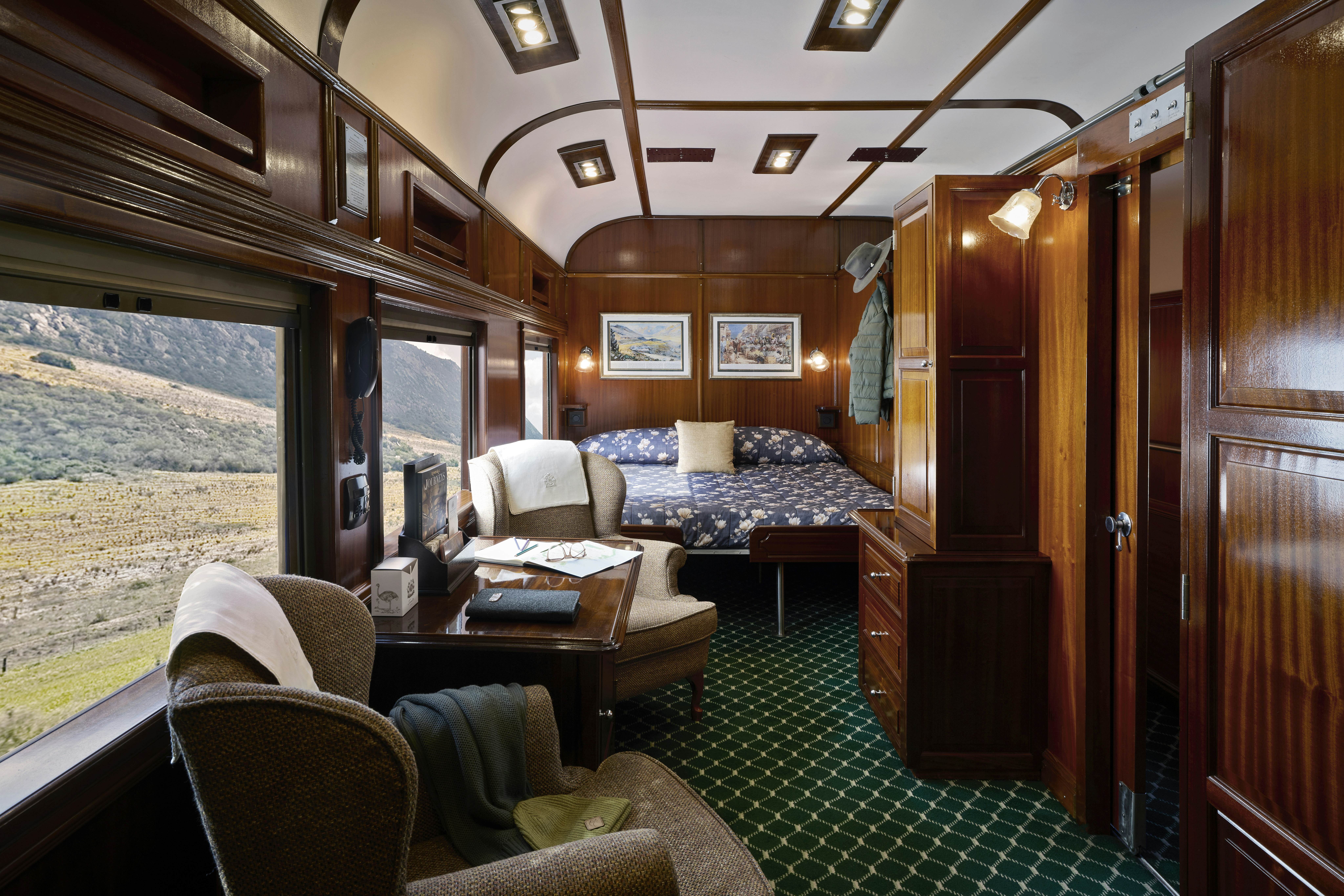 A suite on a train, with a large double bed and a small sitting area near a large window