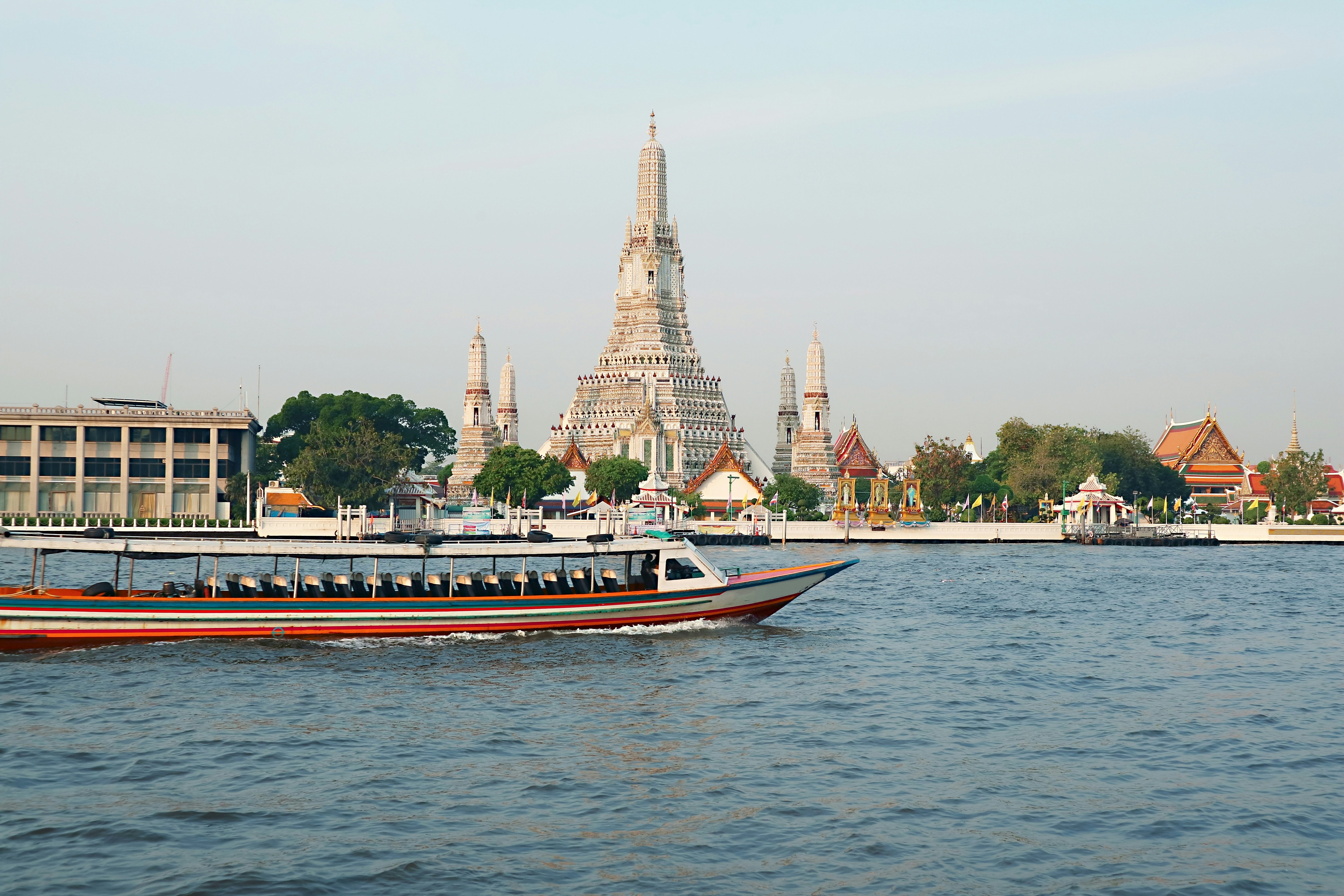 A passenger boat traveling down a river passes a large white temple.