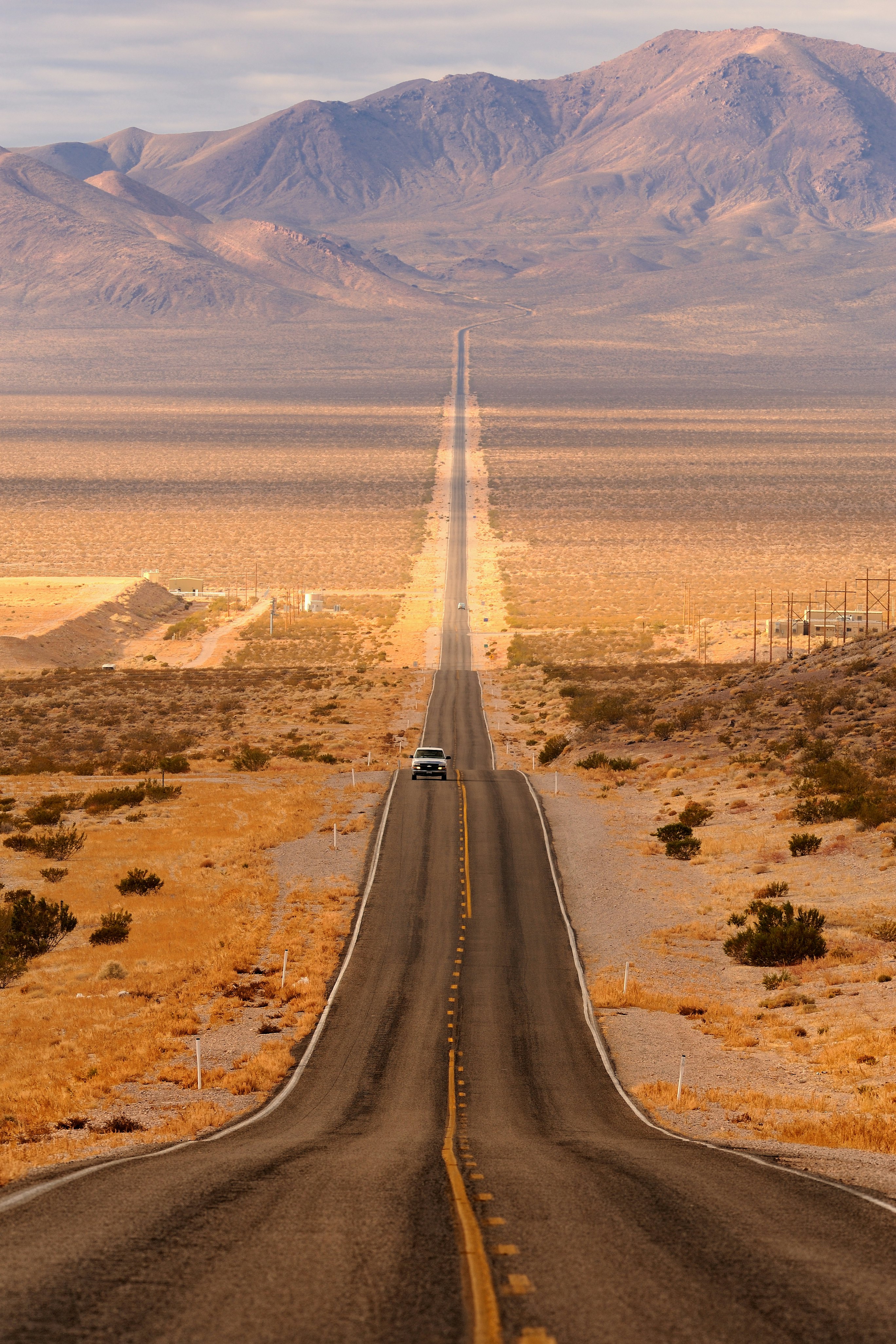 A four-wheel drive on an undulating single-lane highway that stretches far into the hills in the distance.