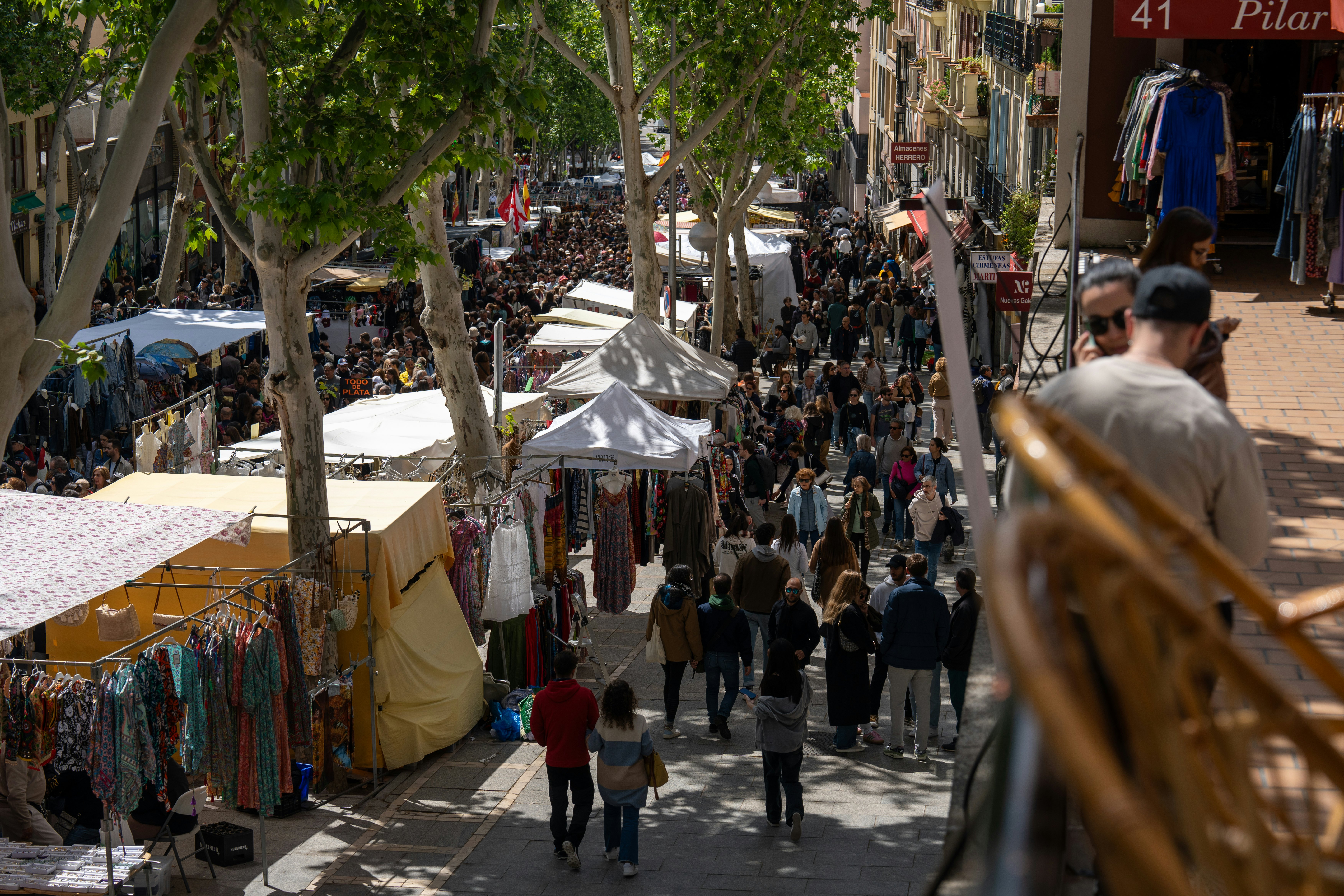 A flea market on a long street is crowded with stalls and shoppers.