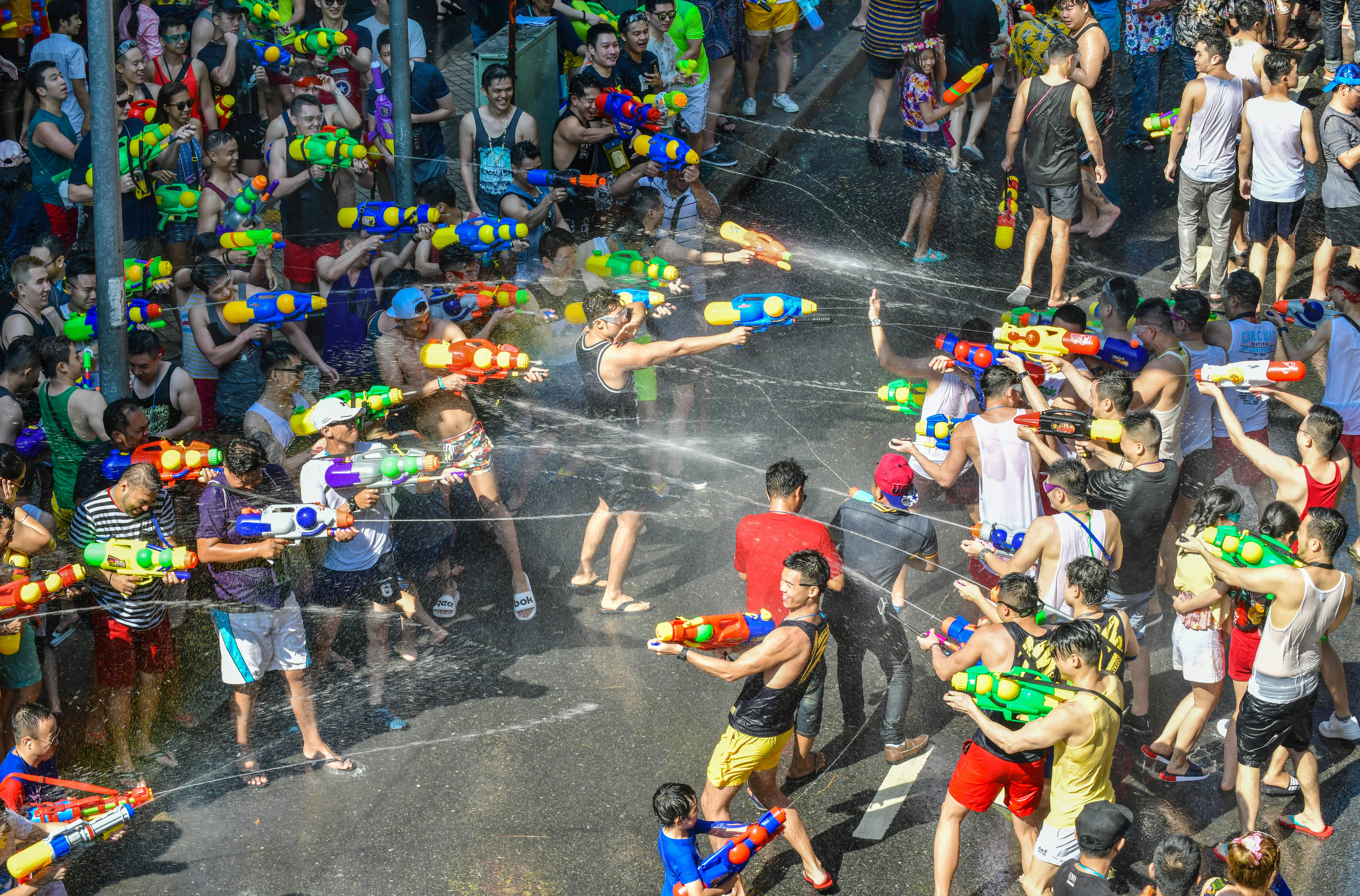 A huge water fight in the street with people armed with water pistols shooting at each other and laughing.
