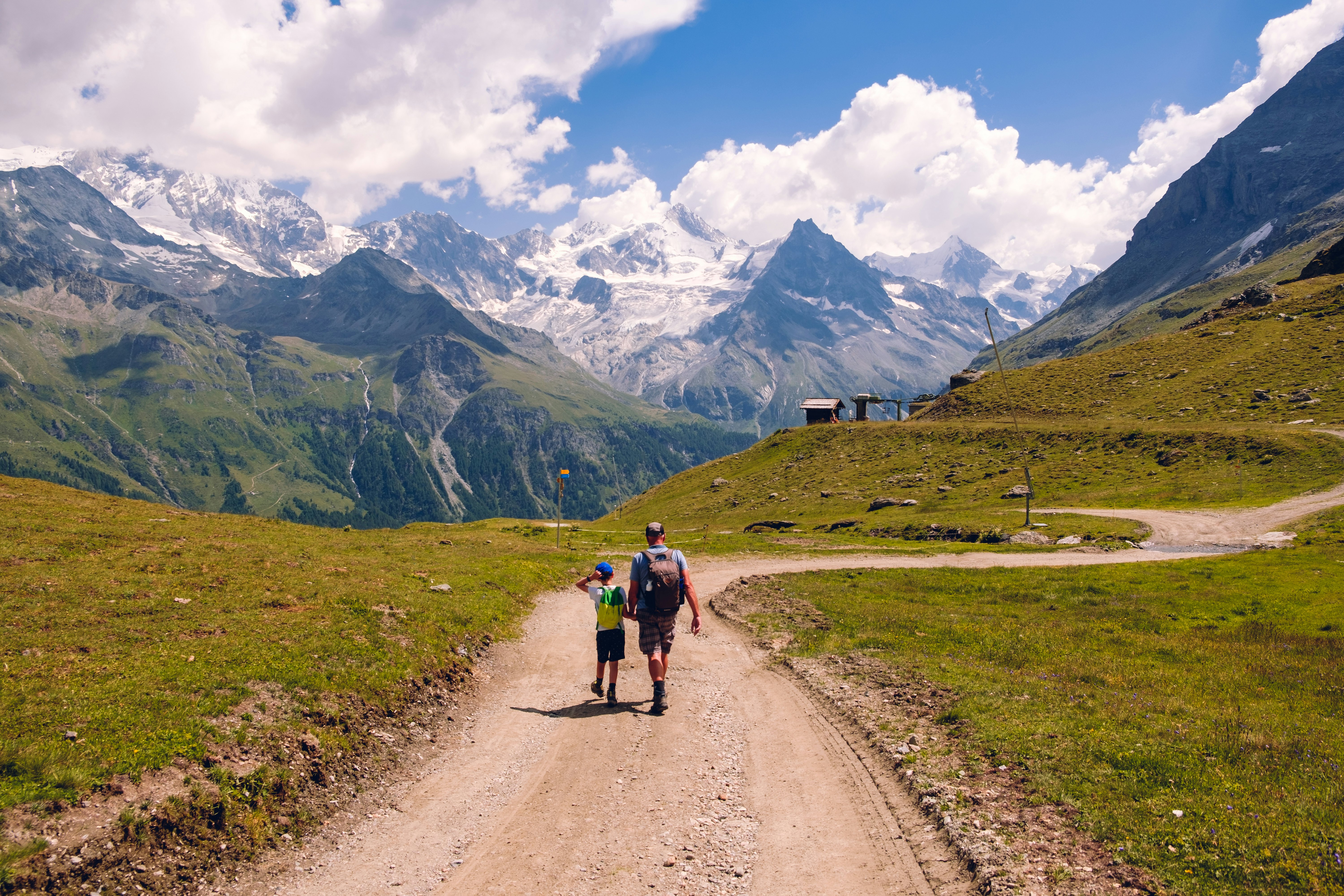 A father and son follow a dirt hiking trail through a mountainous region.