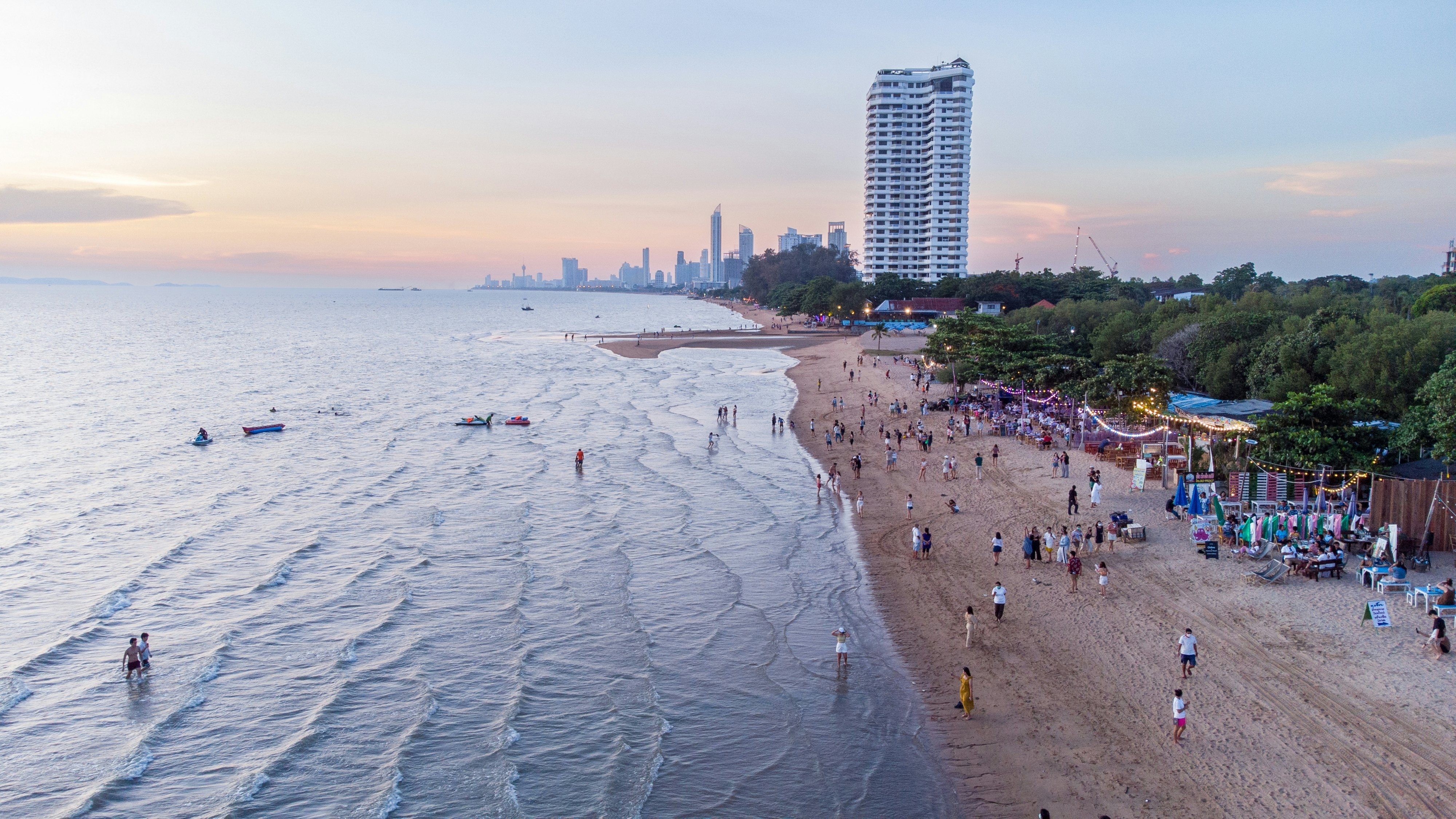 Tourists in the water and sands of a strip of beach near city buildings