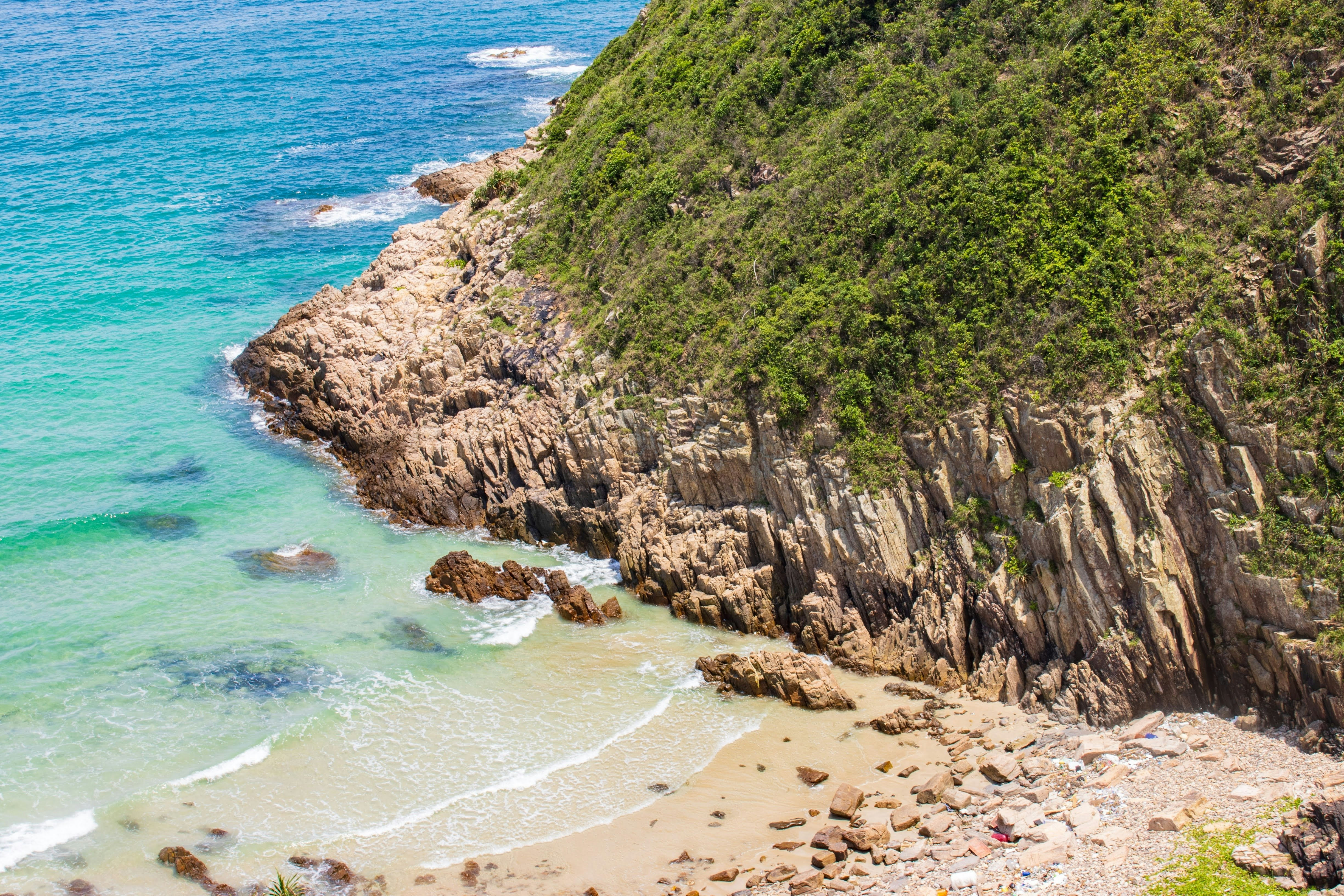 A view down to a rock-strewn tropical beach surrounded by cliffs.
