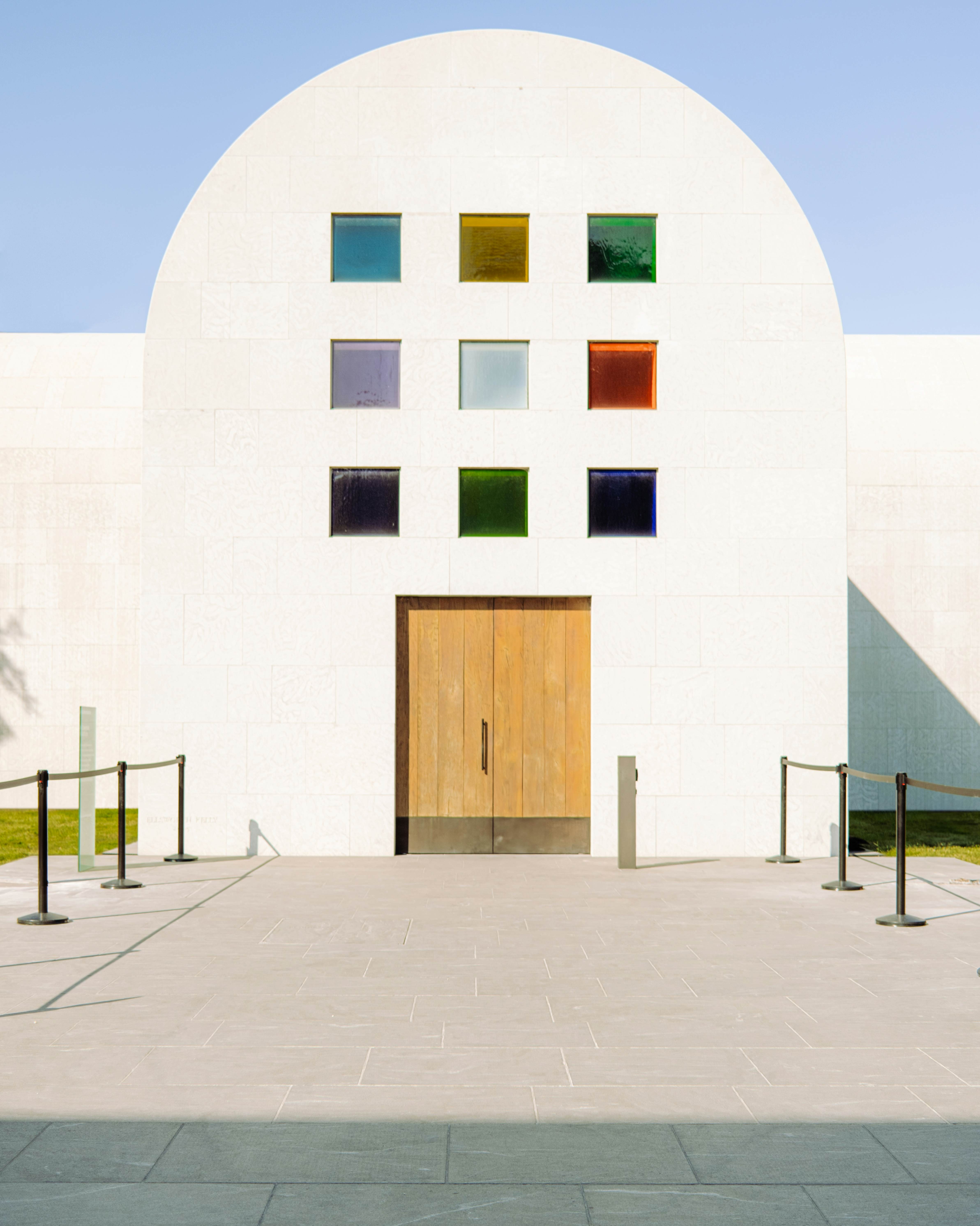 A white building with nine mulitcolored squares above a double wooden door.