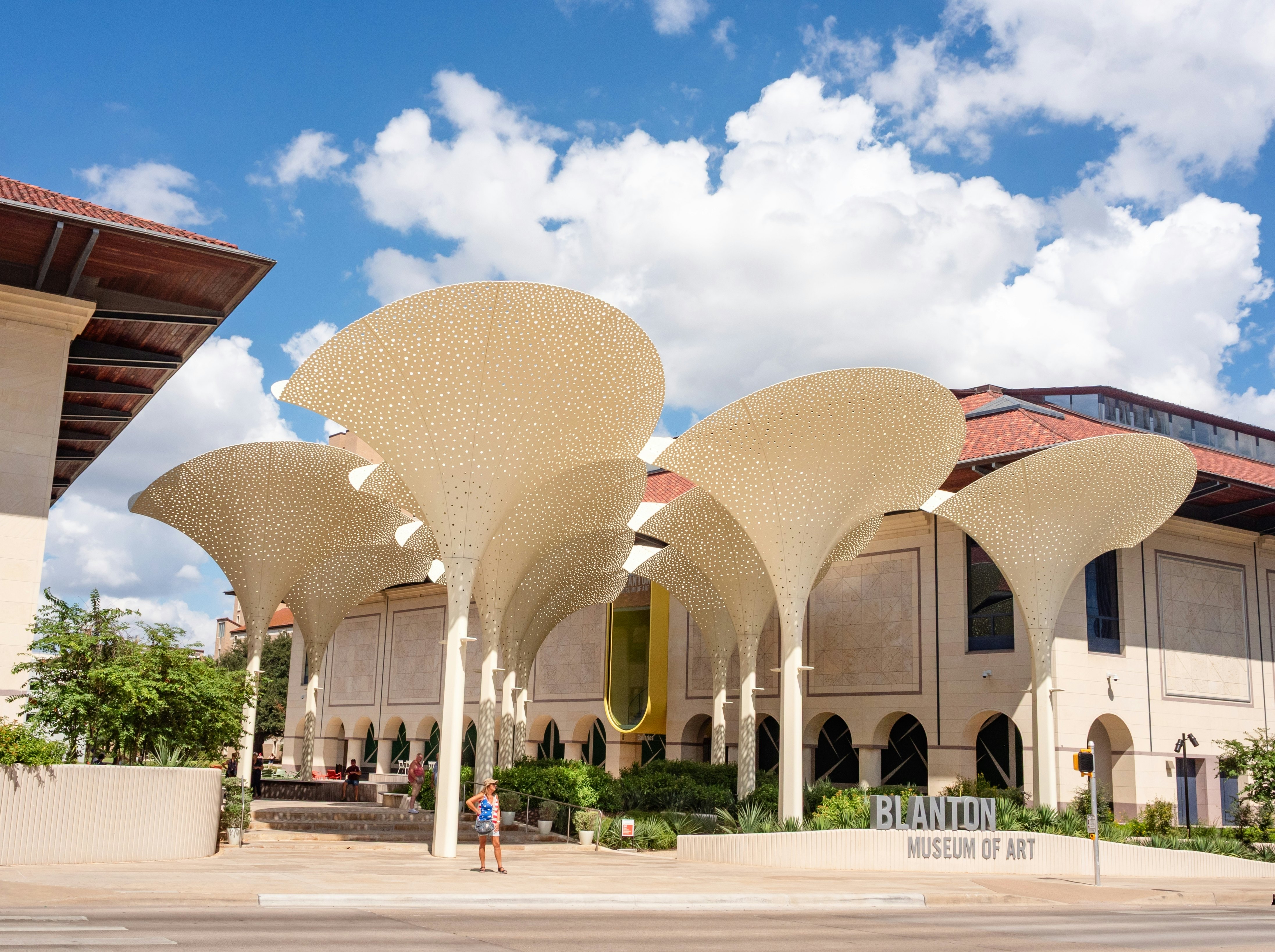 A woman stands in front of fan-topped columns in front of a modern museum building.