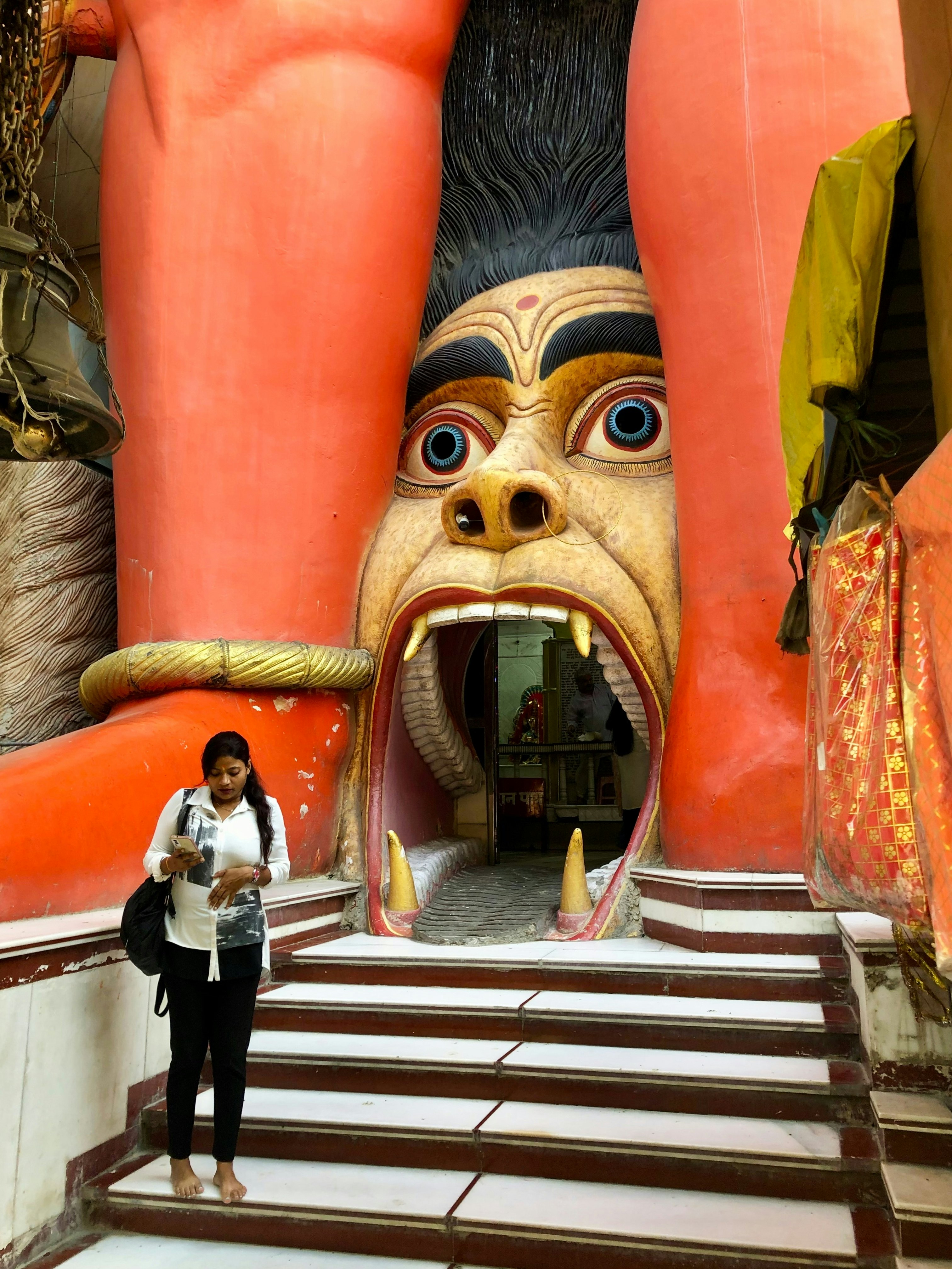 A woman stands near the open mouth of a demon forming the entrance to a temple.