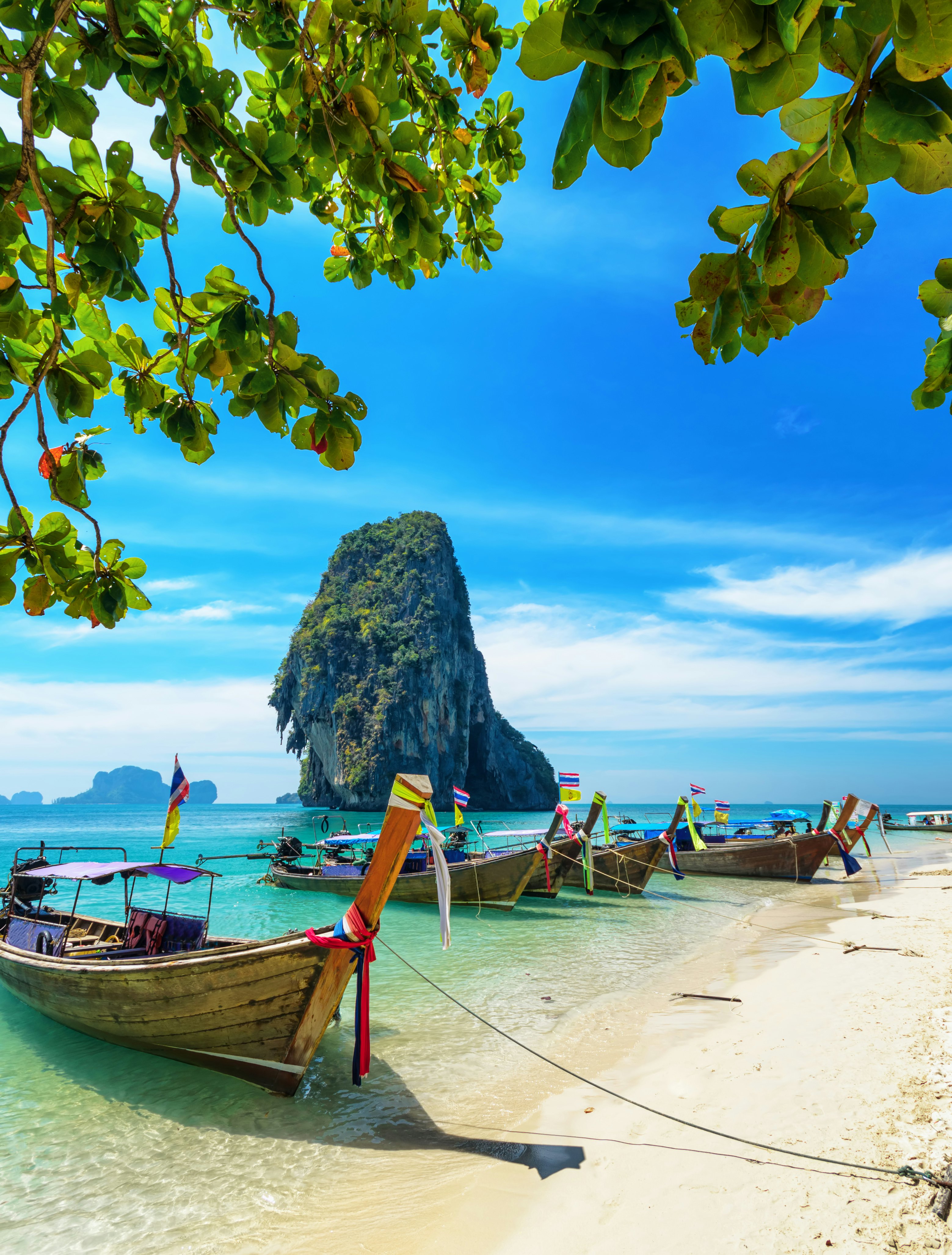 Wooden boats with colorful ribbons wrapped around the bow docked on a white-sand beach lapped by turquoise ocean.