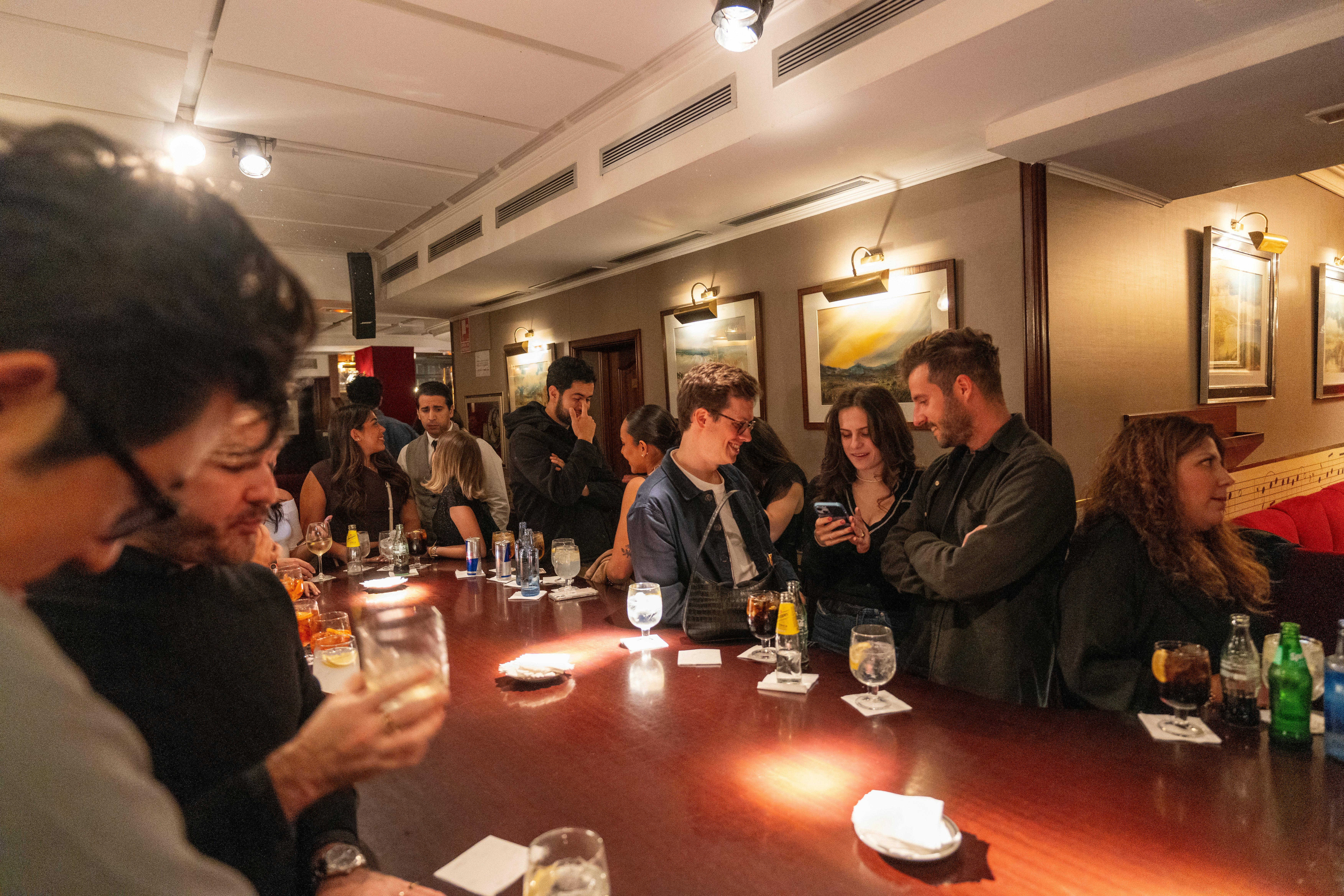 People stand on either side of a long bar with drinks on it.