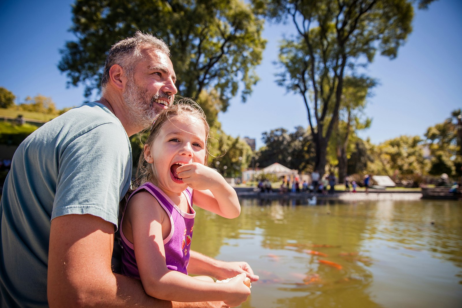 A father and daughter sit next to a pond with koi fish in it at Parque Centenario in Buenos Aires, Argentina