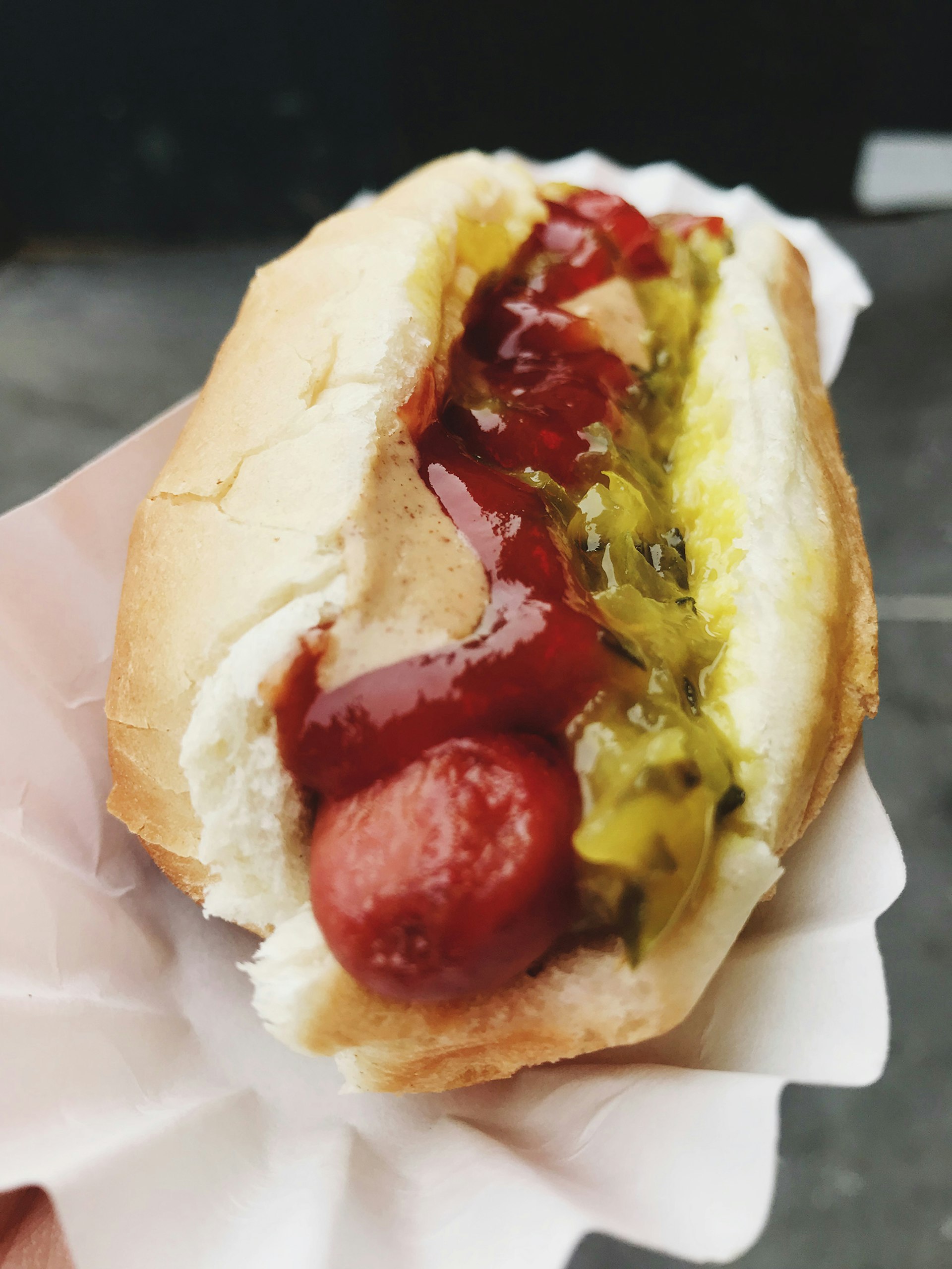 close up of a hot dog in a bun with relish, mustard and ketchup