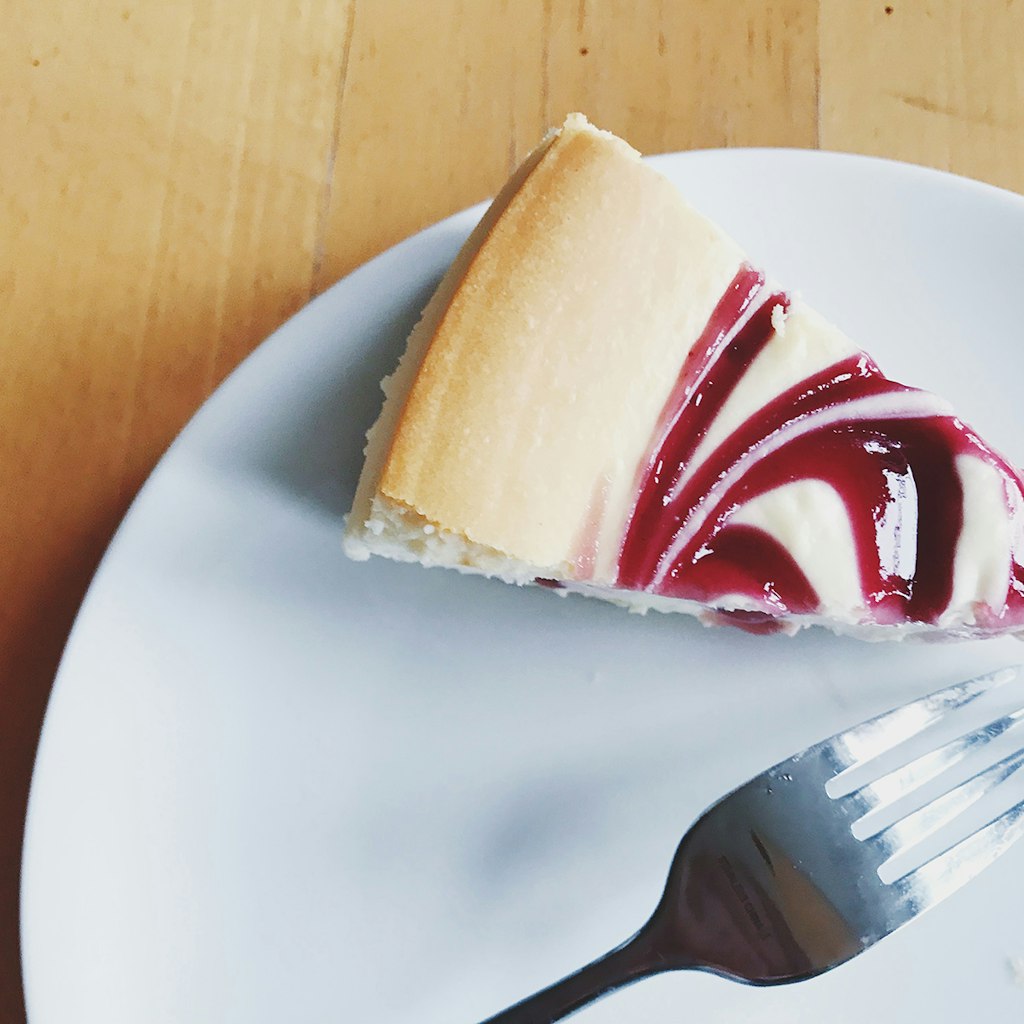 slice of raspberry swirl cheesecake and a fork sit on a plate