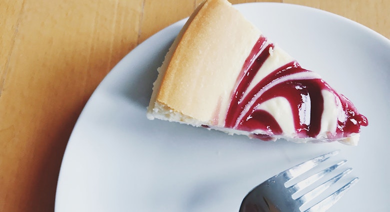 slice of raspberry swirl cheesecake and a fork sit on a plate